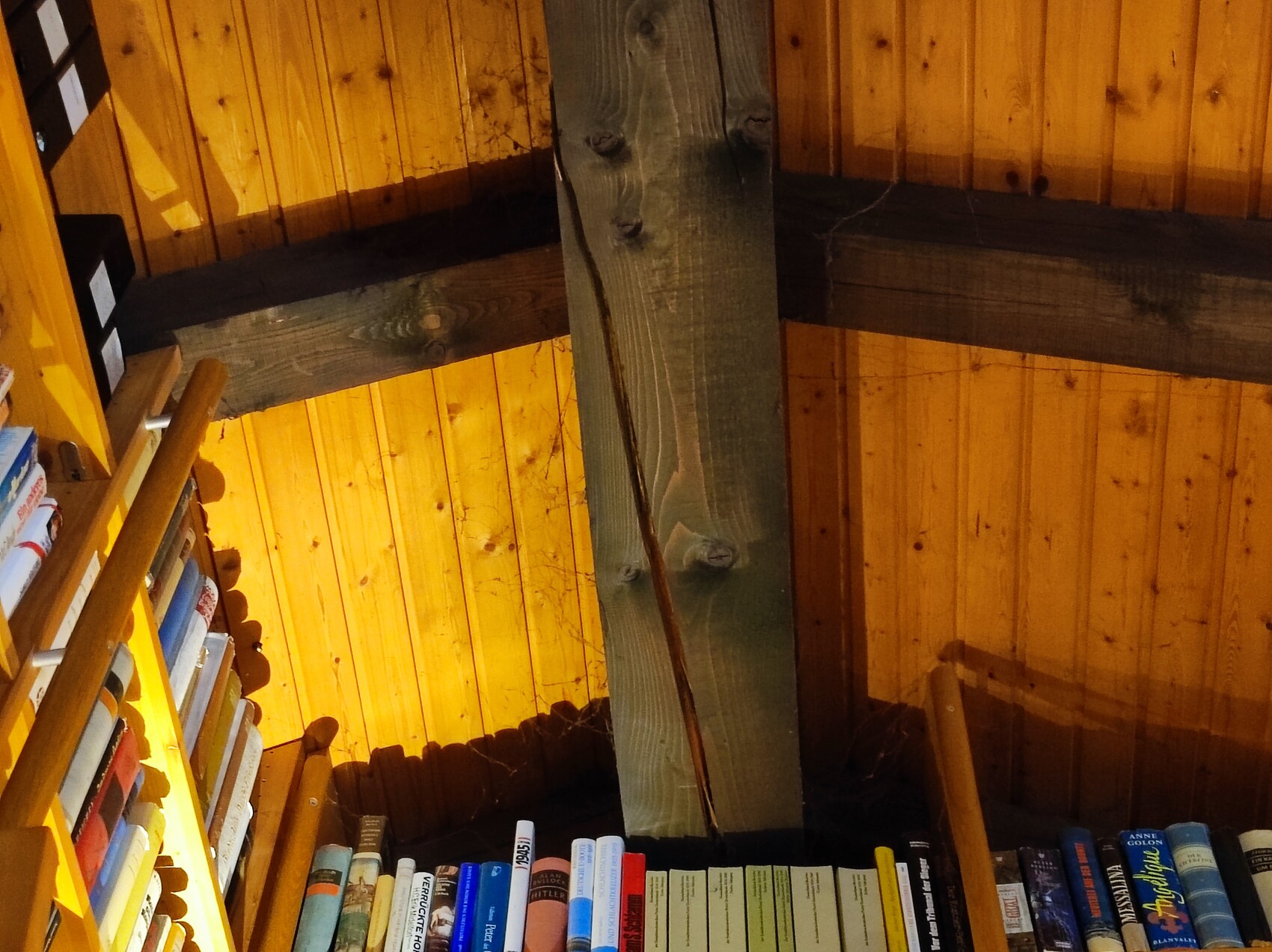 Cozy attic with central wooden beam and bookshelf full of books under warm lighting.