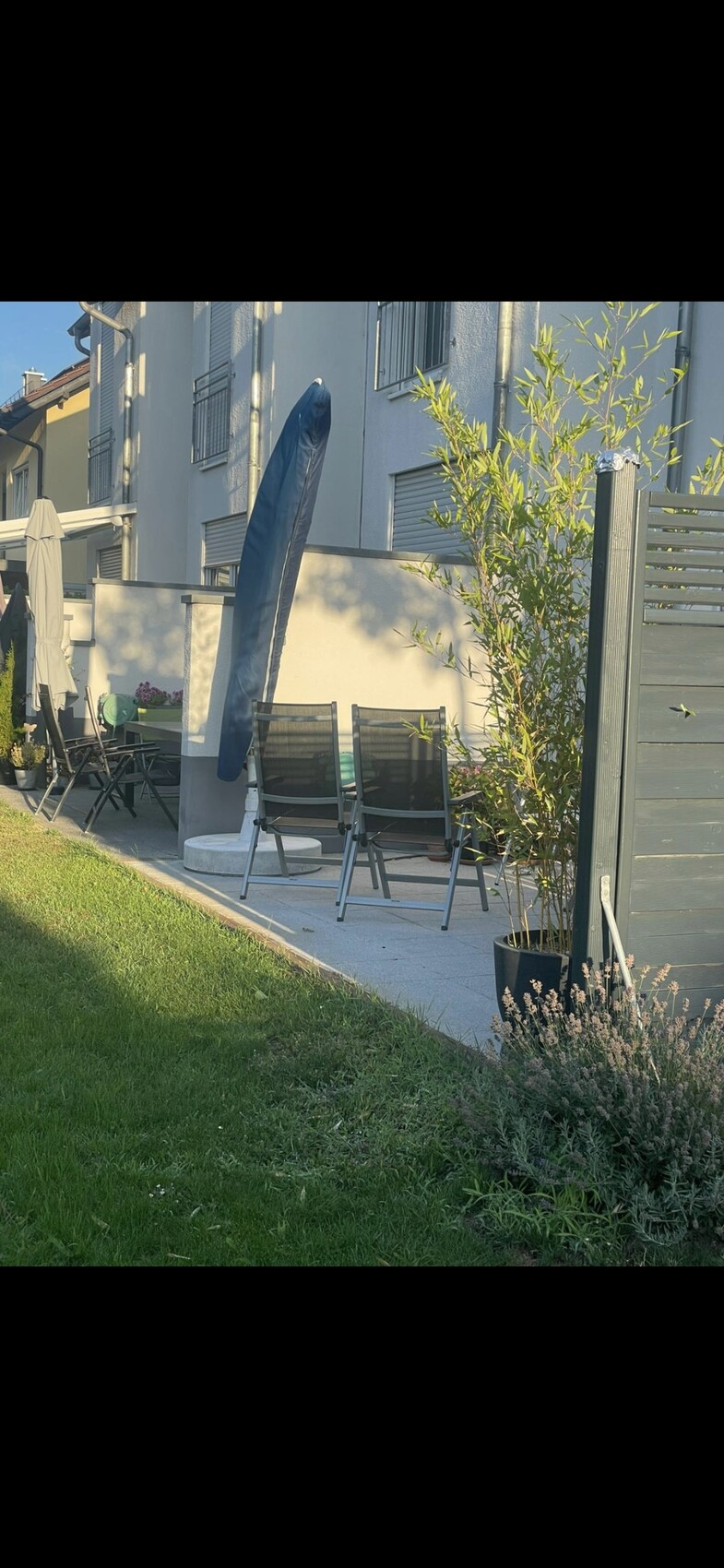 Garden terrace with black folding chairs, blue parasol, planters, and grass in front of the house.