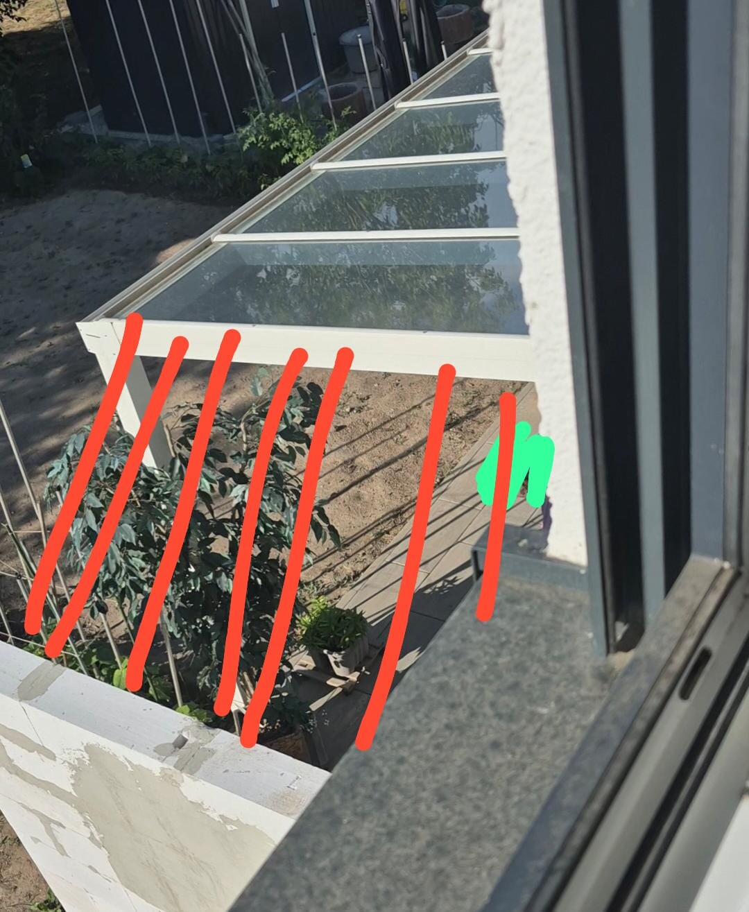 View from inside onto balcony with glass roof structure and plants underneath.