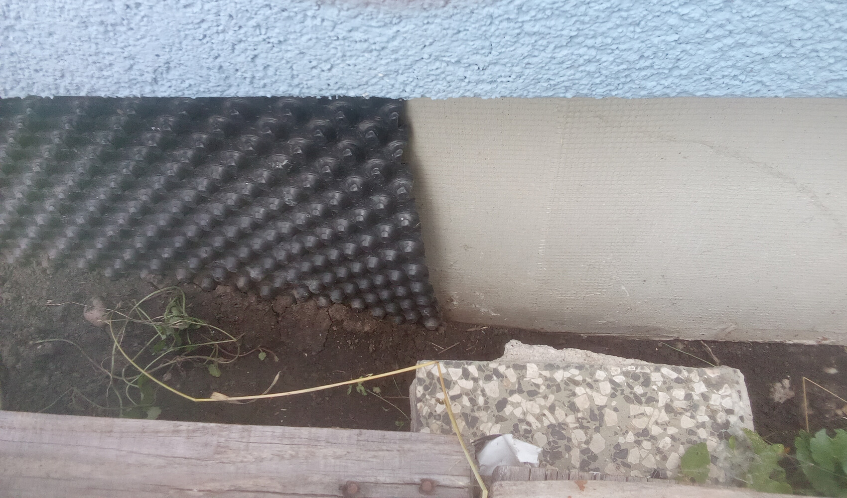 Exterior foundation wall with drainage mat, soil visible.