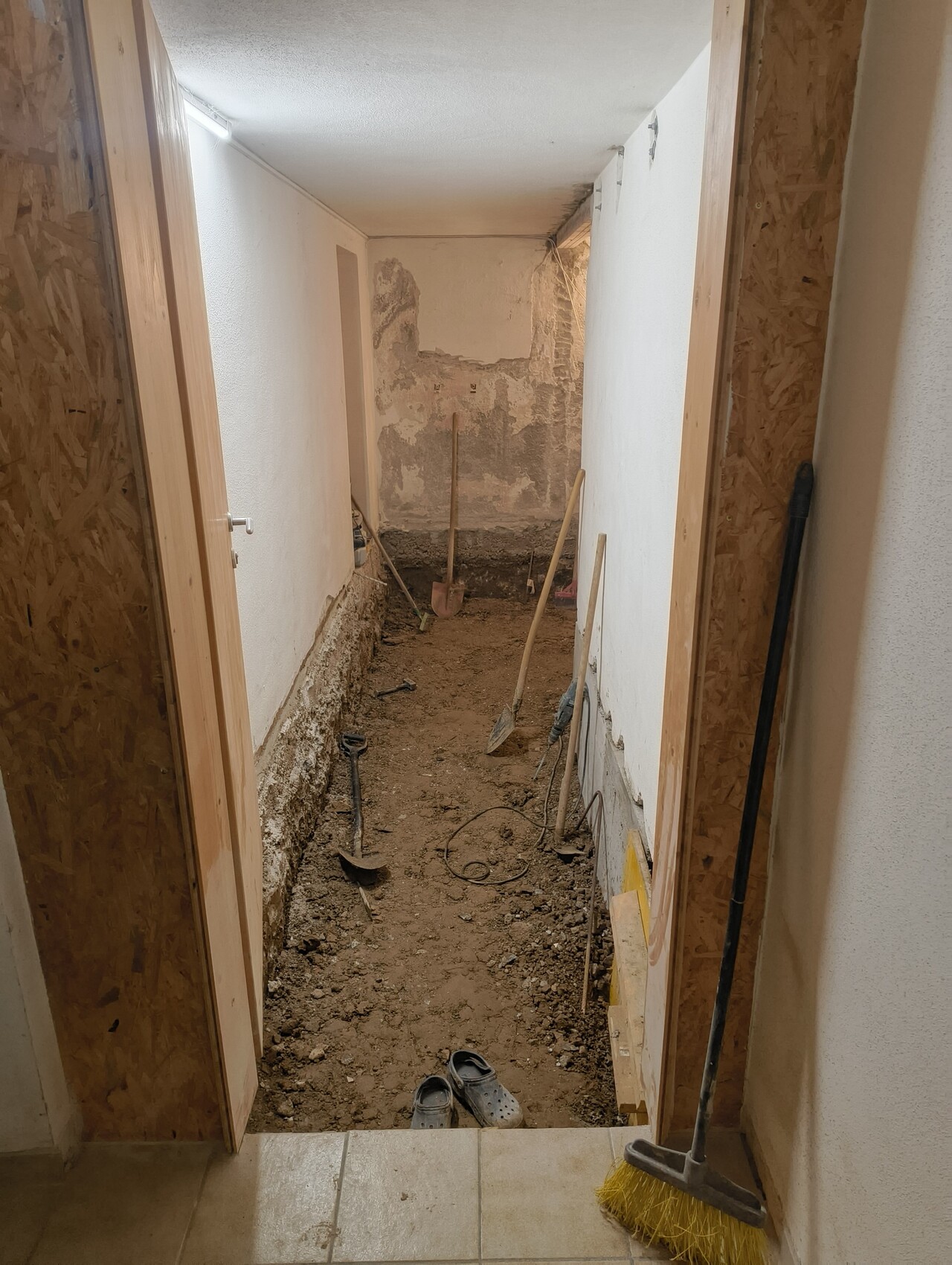 Corridor under renovation with exposed soil surface, shovels, and brooms as tools.