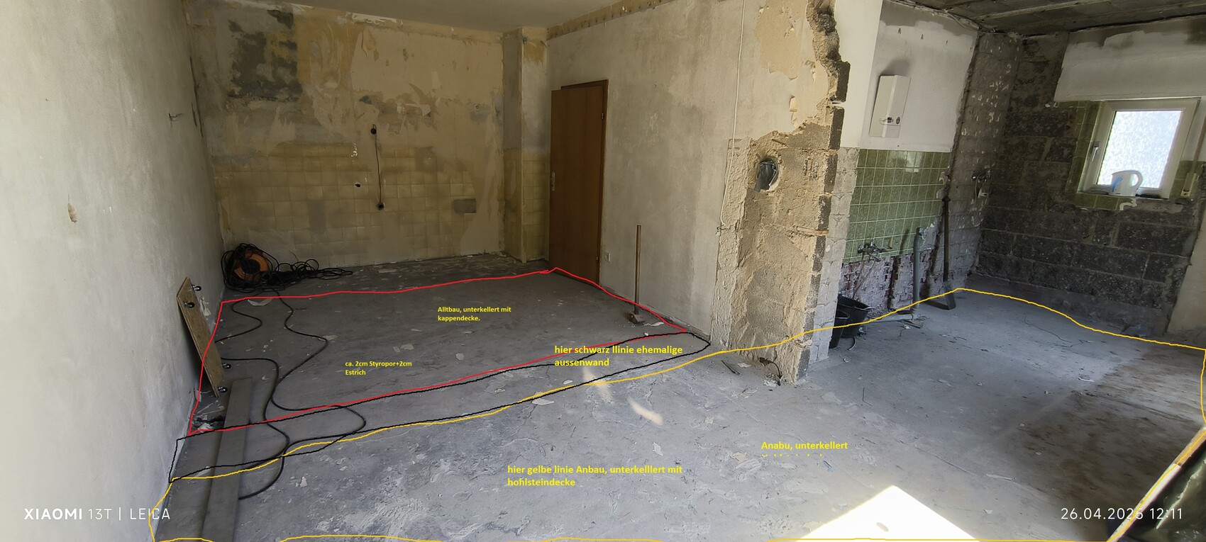 Basement room in shell condition: exposed walls, green tiles on the right, door in the middle, cables on the floor.