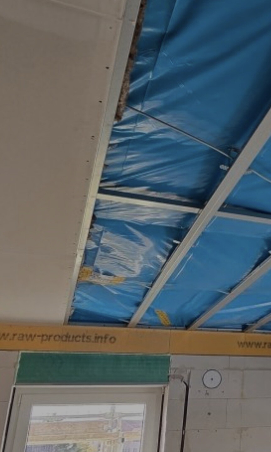 Construction renovation: open ceiling with blue insulating foil, metal beams; door visible below.