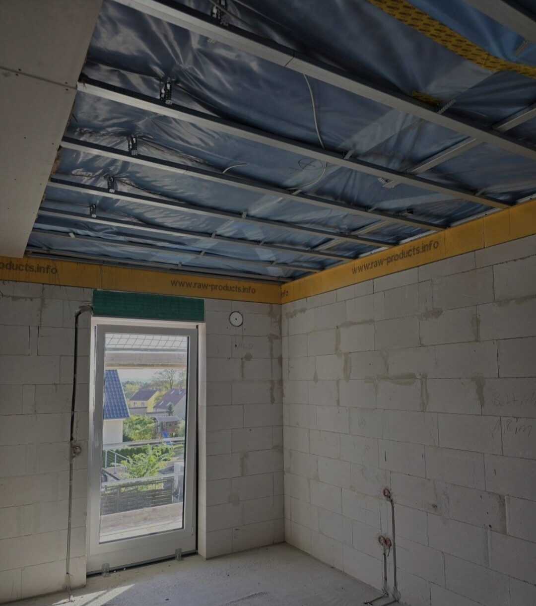 Unfinished interior with open ceiling, blue insulation and yellow construction tape; door leading outside.