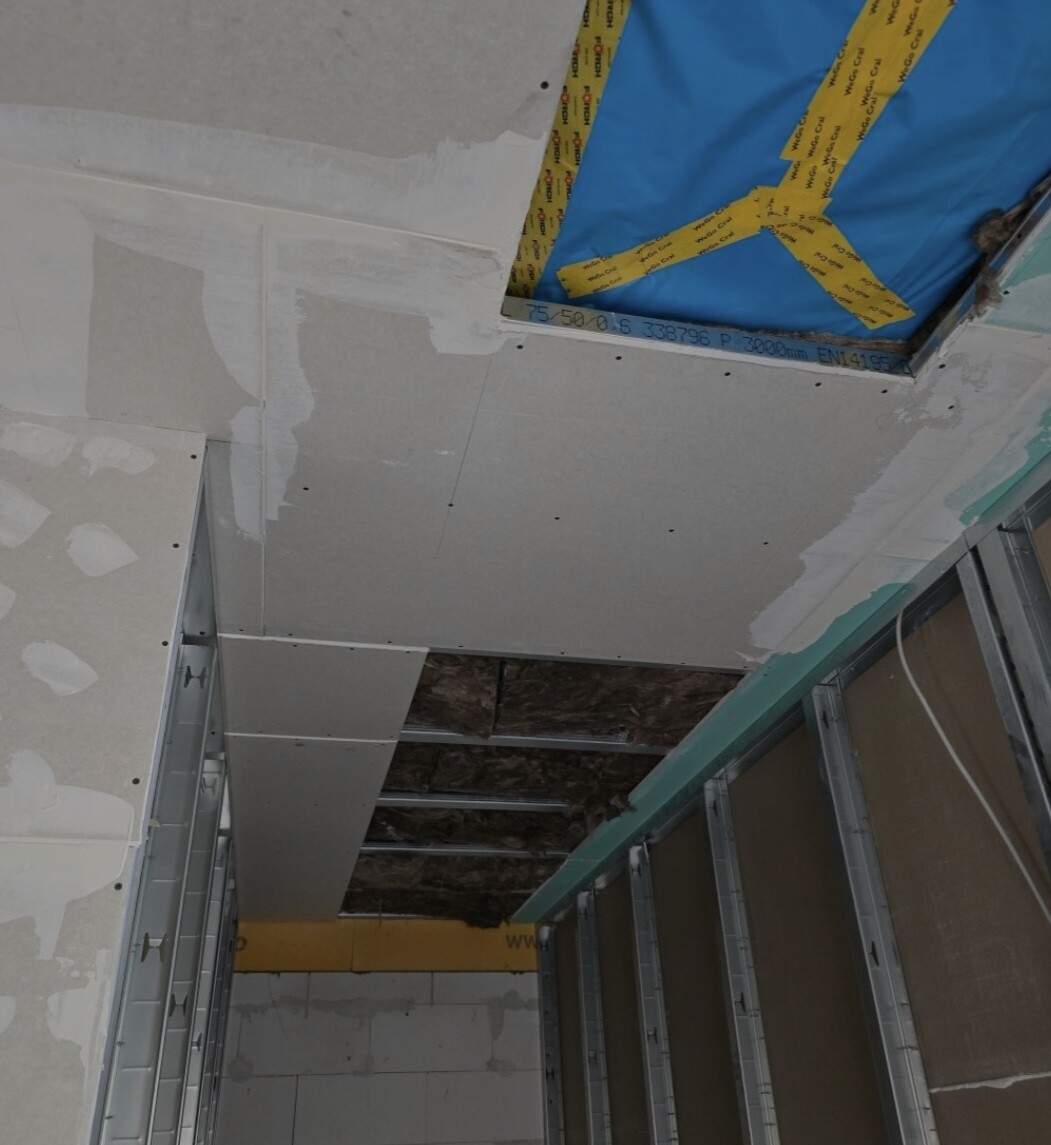 Construction site: ceiling made of drywall panels on metal studs, open hole with blue cover.