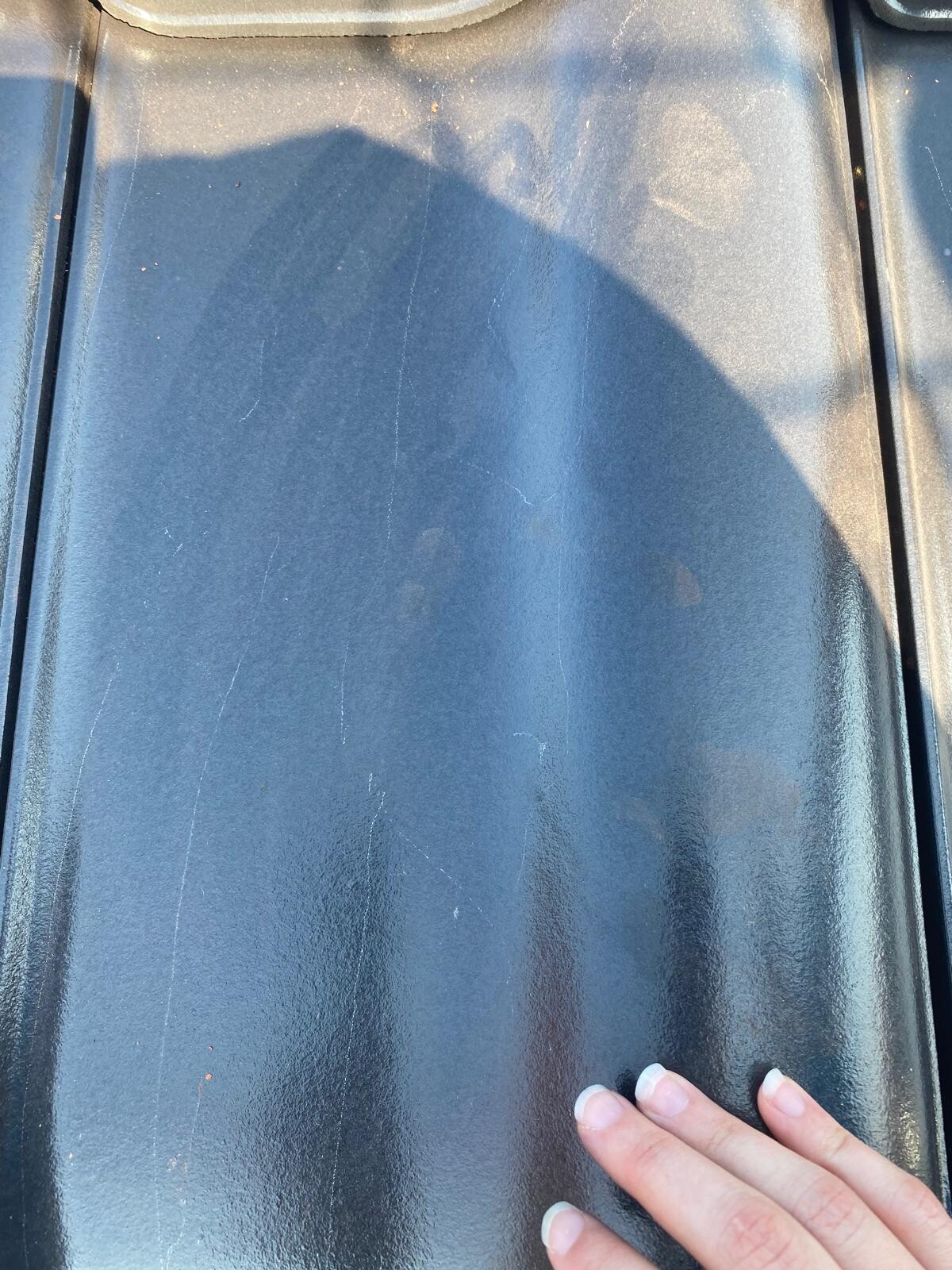 Close-up of a blue metal roof panel with scratches; a hand touching the edge
