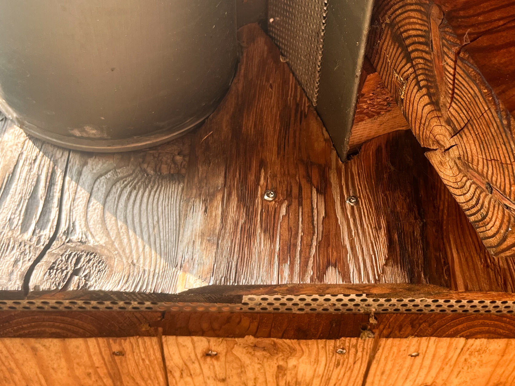 Wood beam ceiling with a round metal container on the left and perforated metal strip at the bottom.