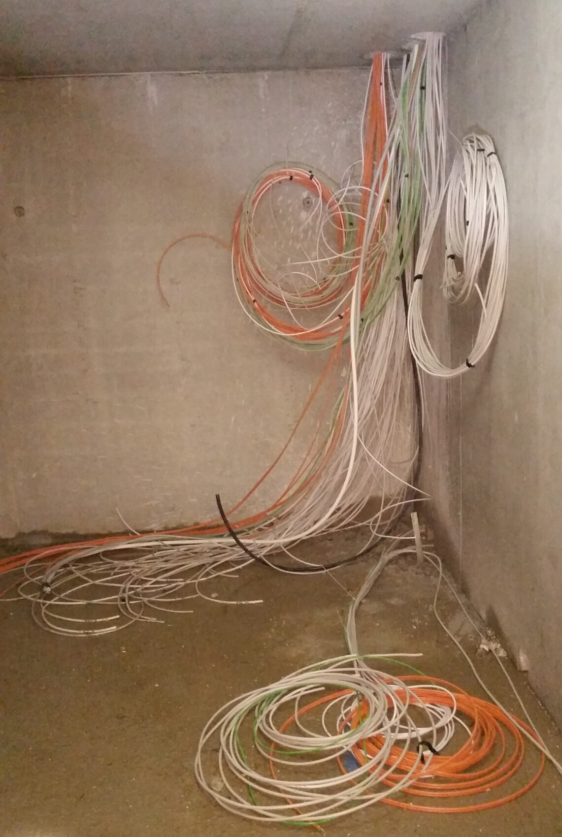 Kabelsalat in Rohbau: weiße, orange und grüne Leitungen hängen an der Wand und liegen am Boden.