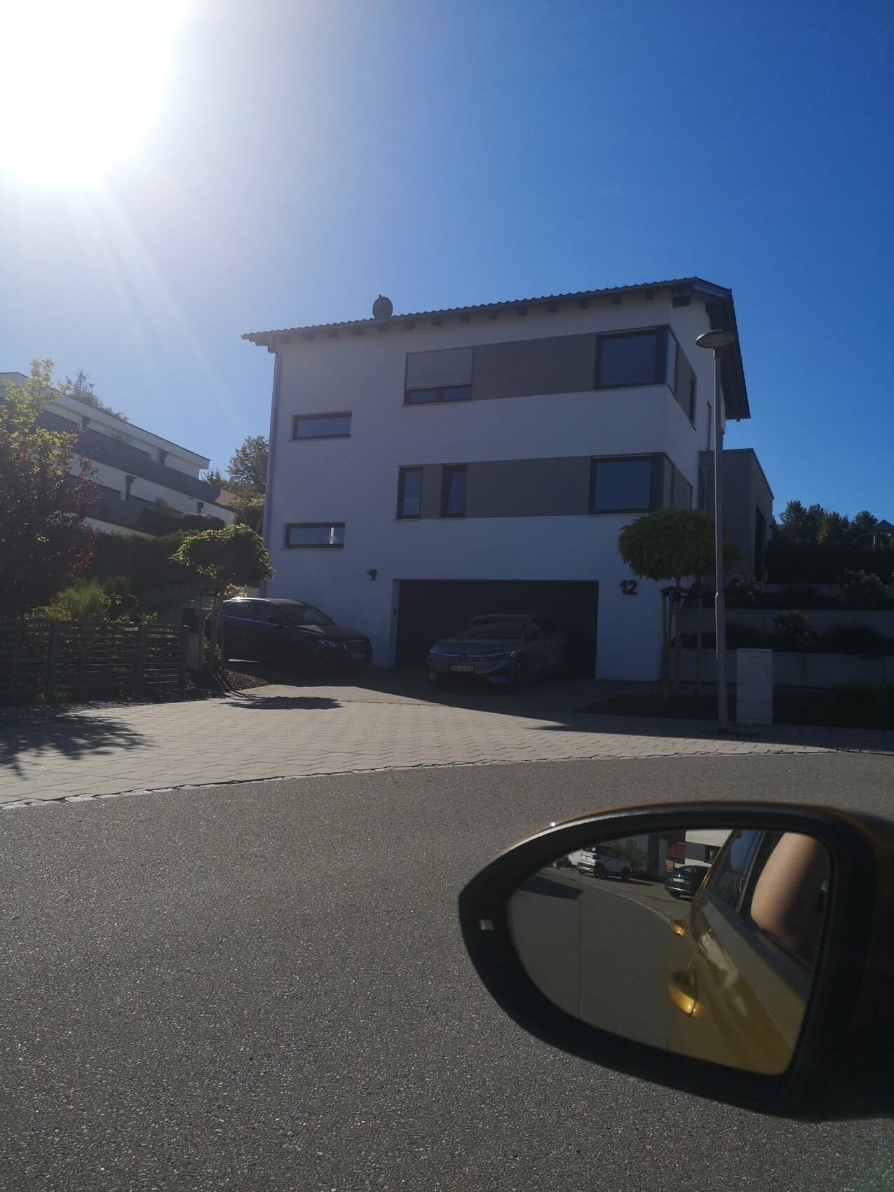 Modern three-story residential building front with garage and parking spaces on a sunny day