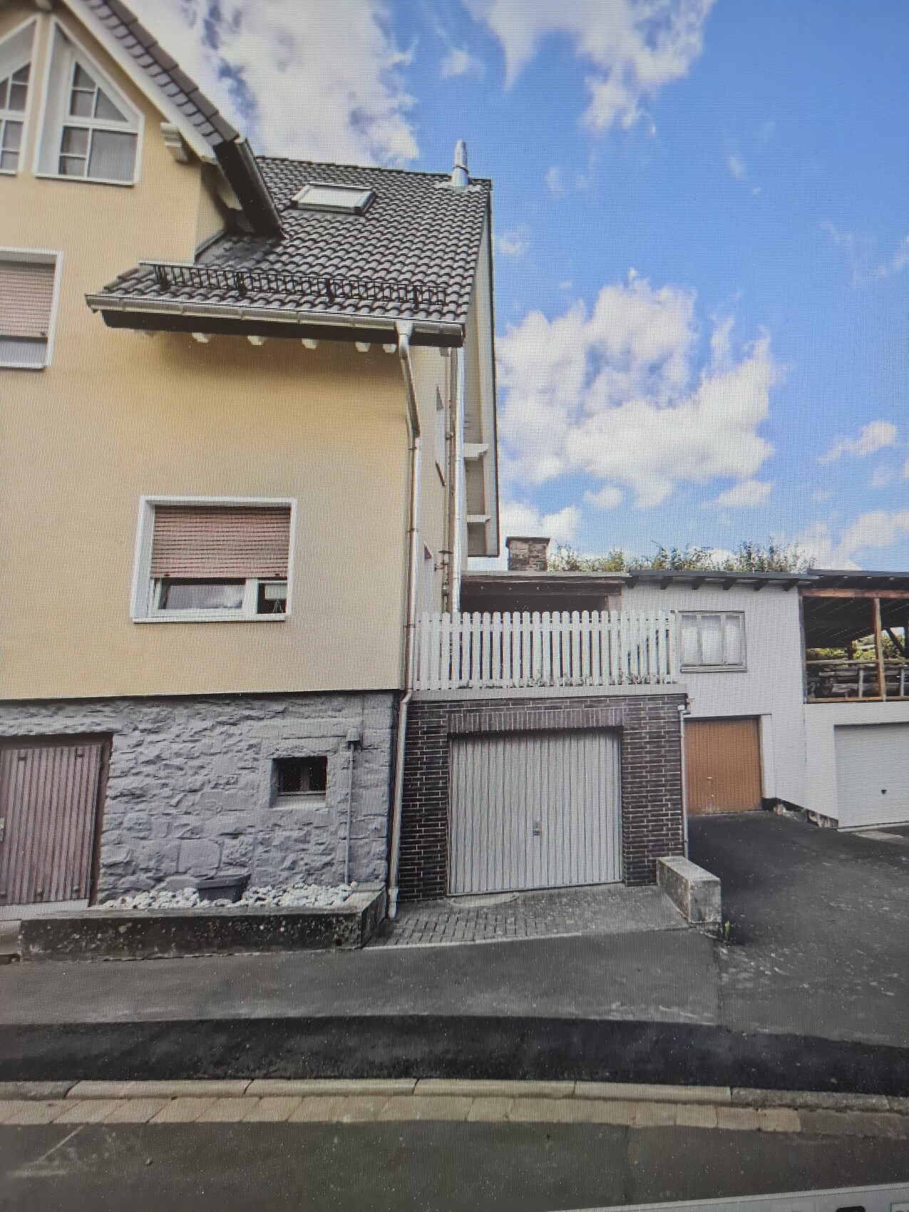 Two-story residential house with garage, stone base, beige facade, and roof tiles.