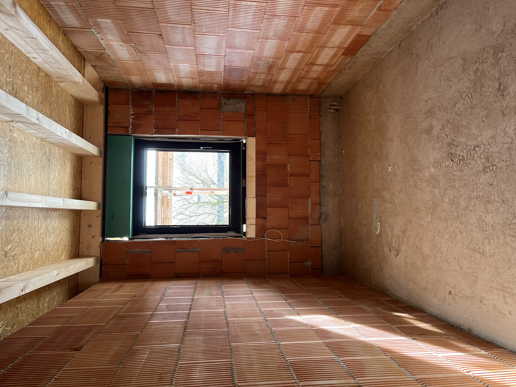 Baustelle: Innenraum-Rohbau mit Backsteinwand, Fensteröffnung und Holzrahmen.