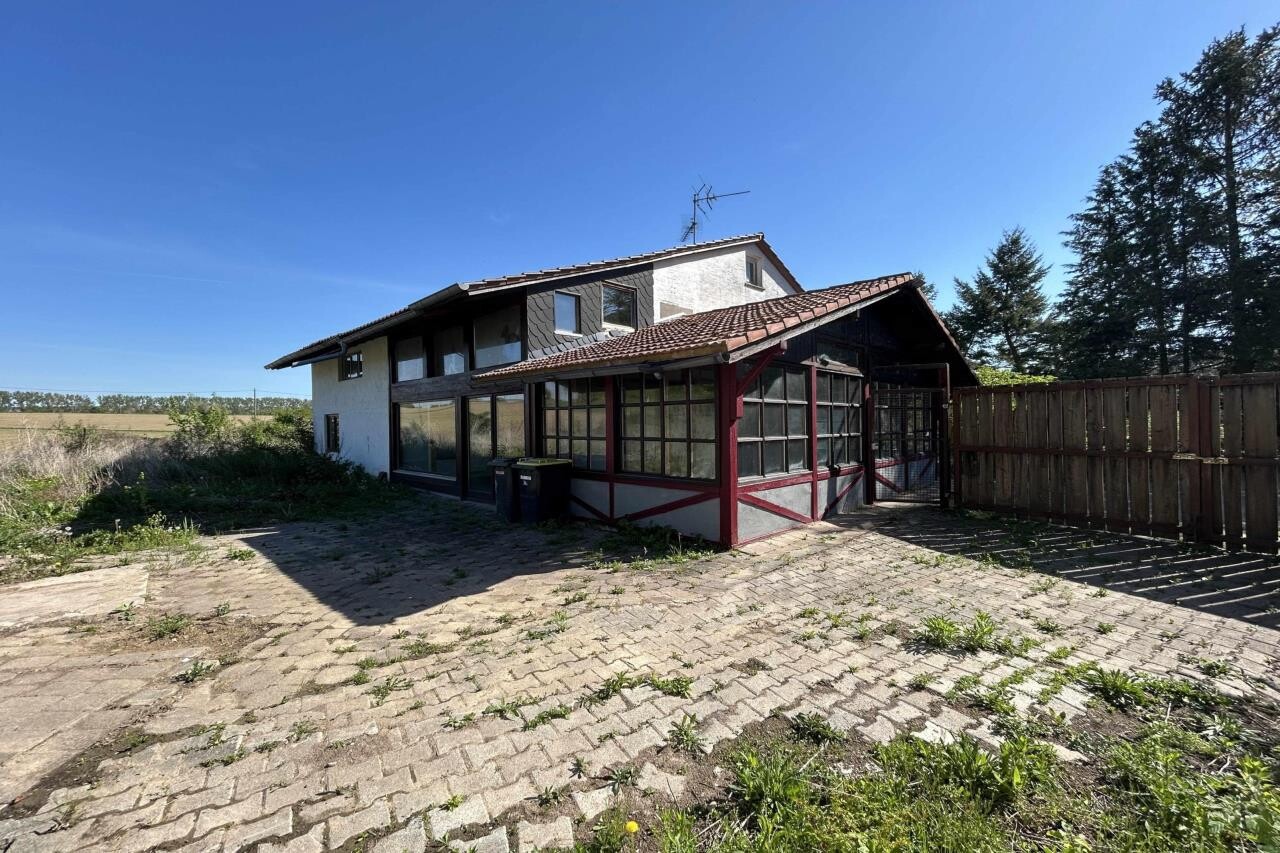 Exterior view of a house with glass veranda, paved yard and fence under blue sky
