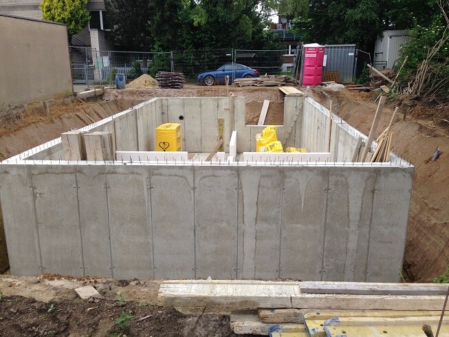 Concrete foundation with interior walls and construction equipment; pink portable toilet in the background