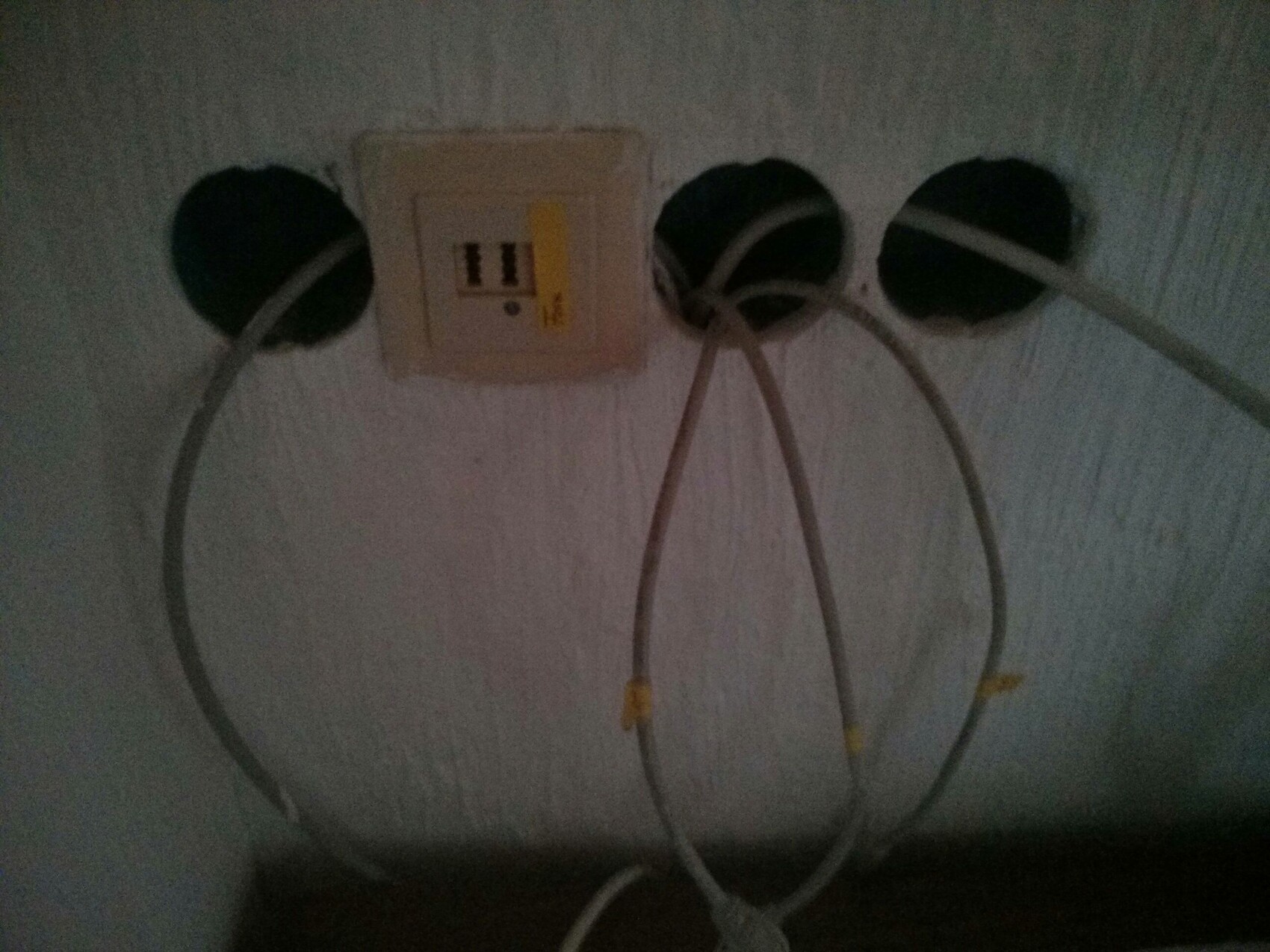 Dark wall installation with three round openings, socket, and cables