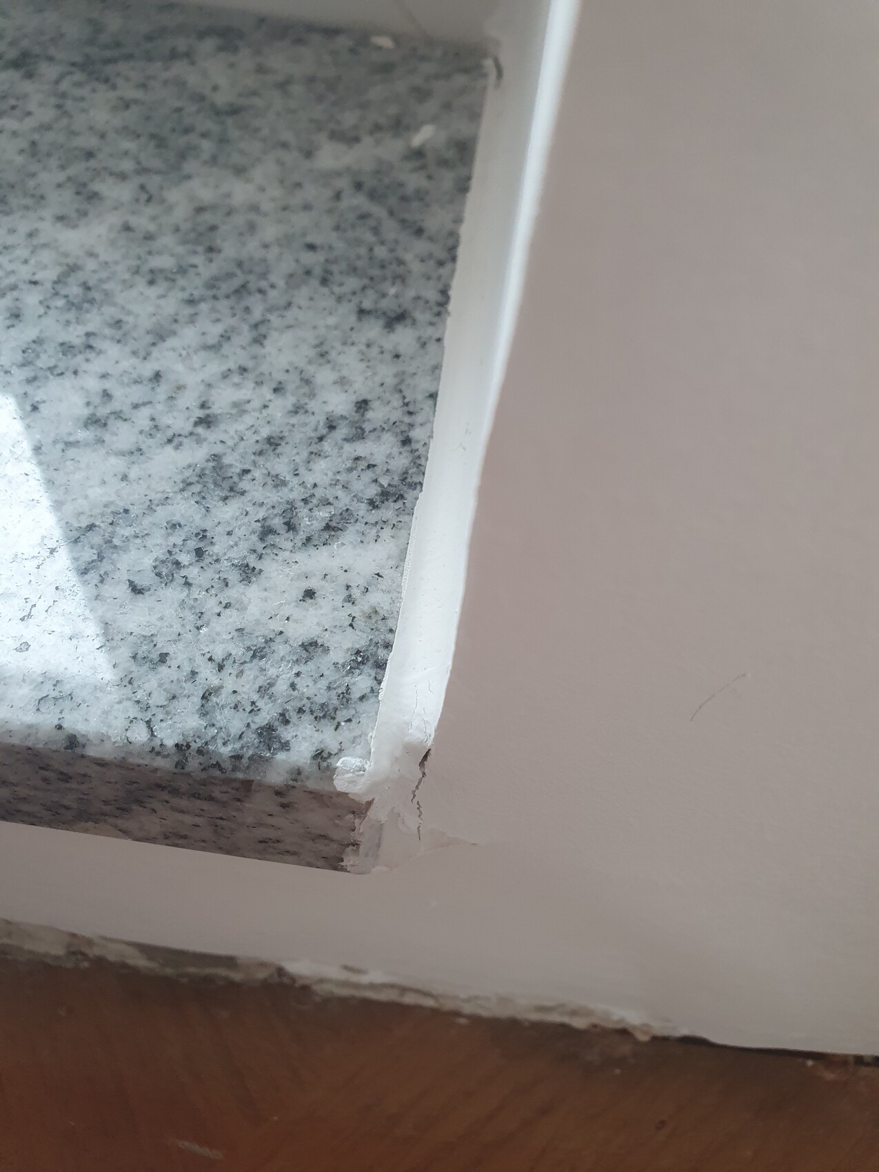 Close-up of a granite kitchen countertop with damaged edge trim next to the wall