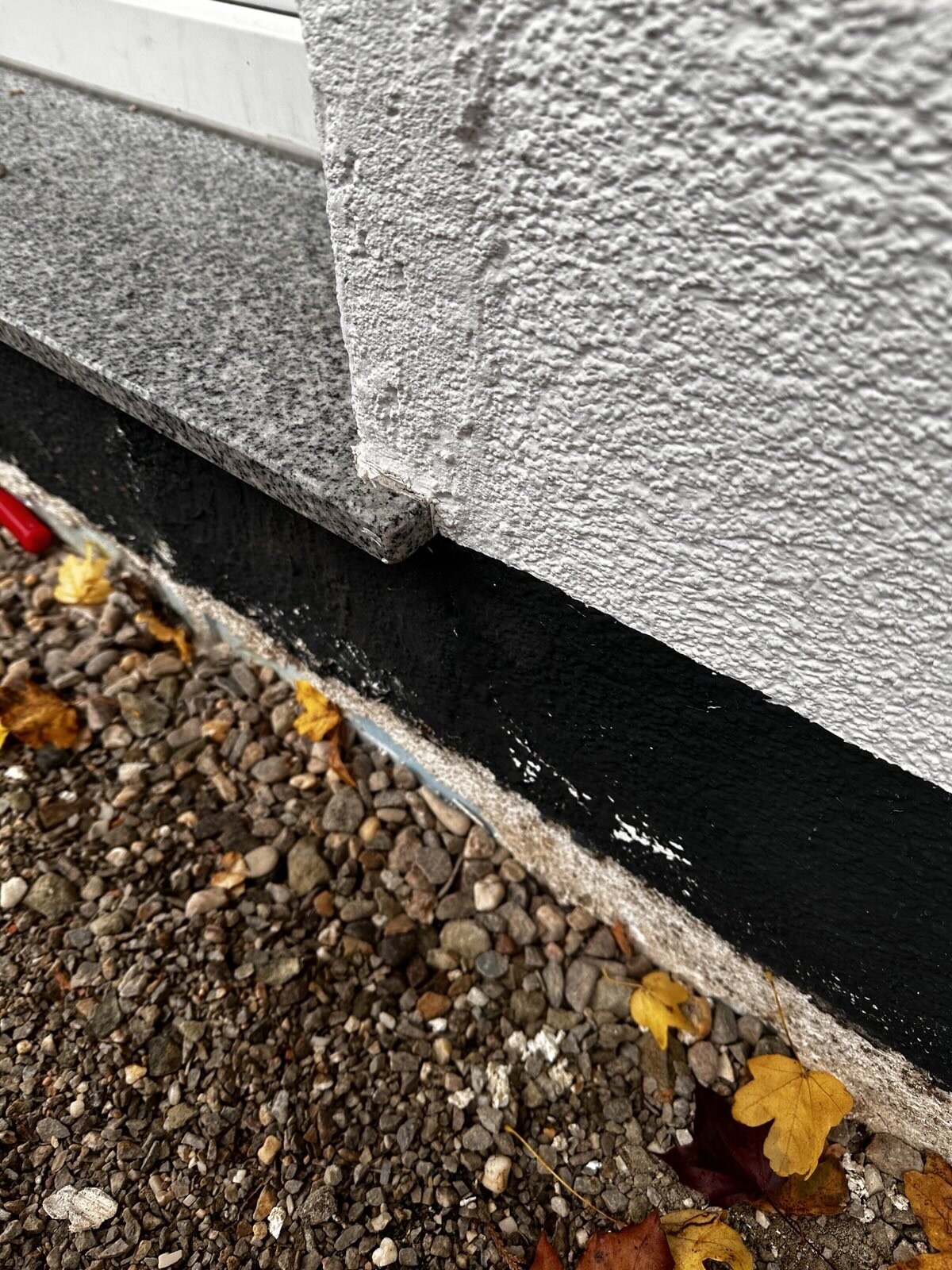 Close-up of a foundation edge with black waterproof coating on the building wall and gravel ground.