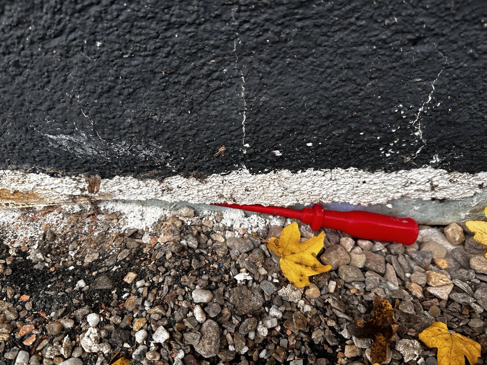Exterior wall with black waterproofing, white joint cracks, gravel, red screwdriver