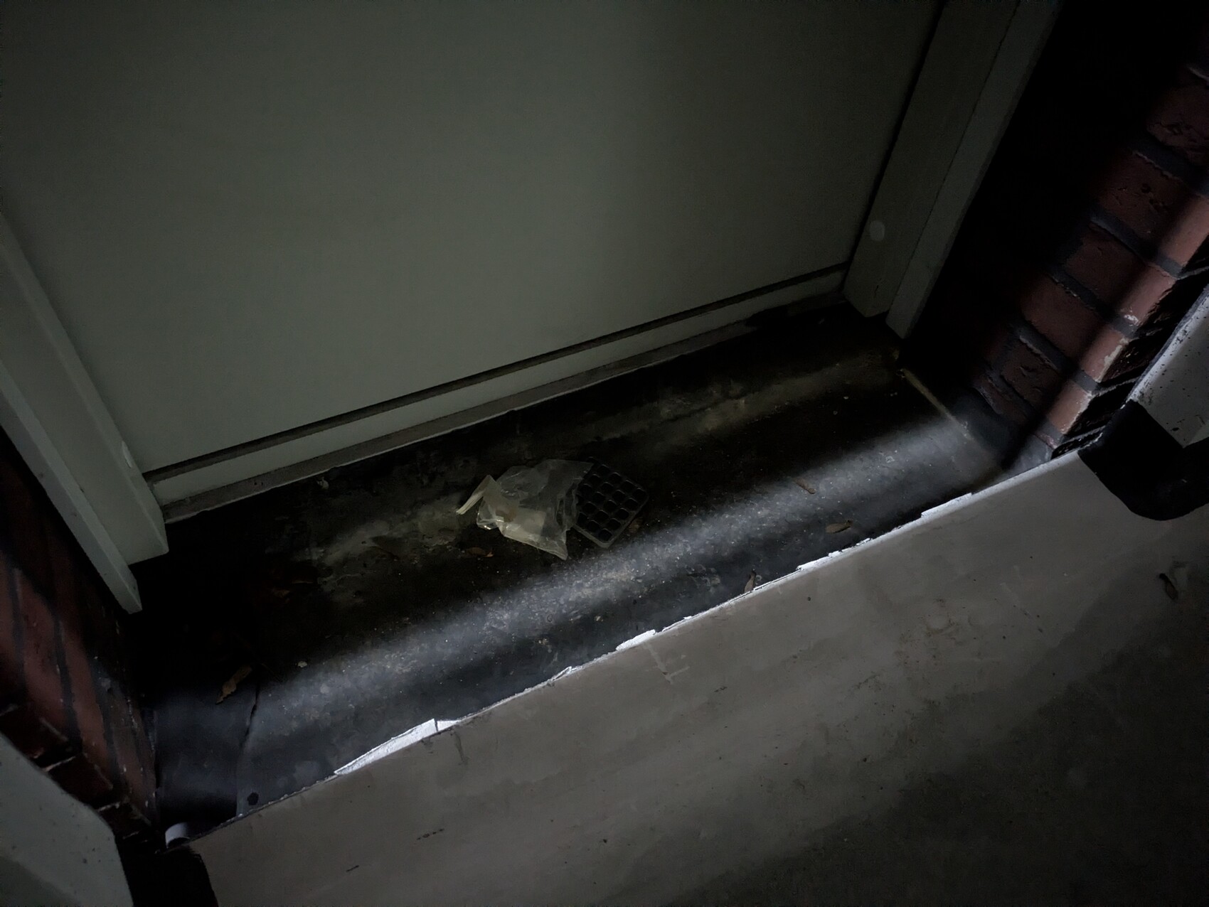 Basement floor with floor drain, dark basement corridor, door frame and brick wall