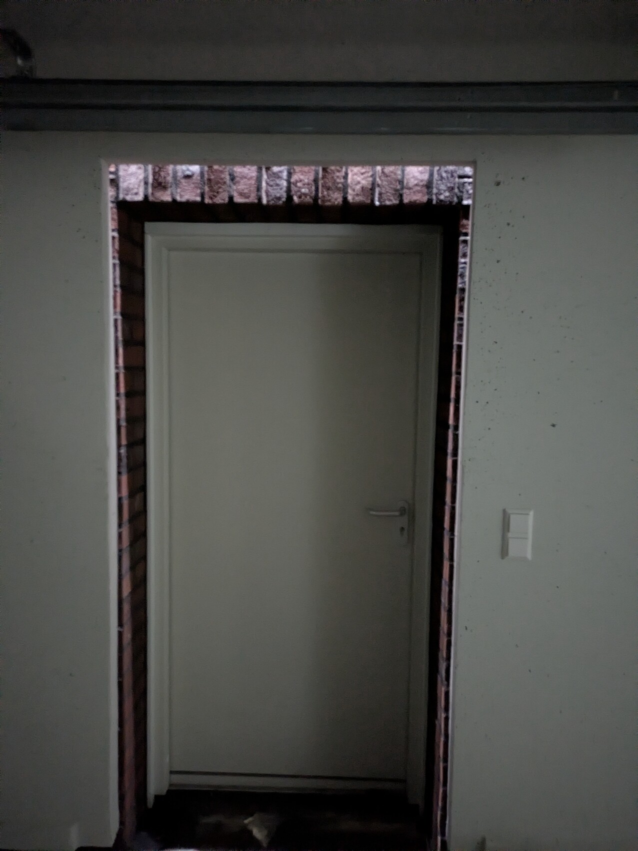 Gray door with brick frame in dark hallway, interior visible