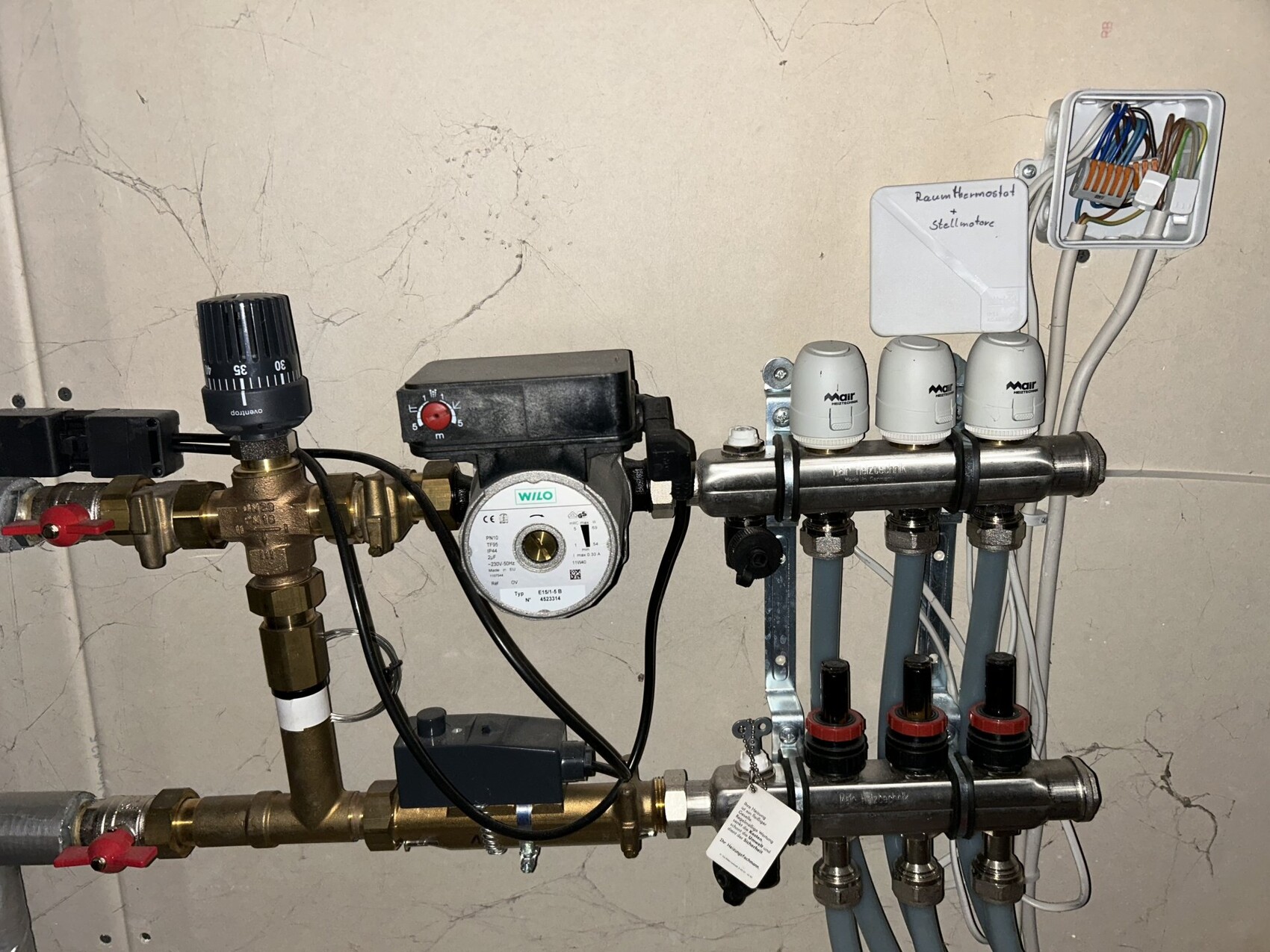 Utility room with heating distributor, pump, valves, and electrical connection on the wall.