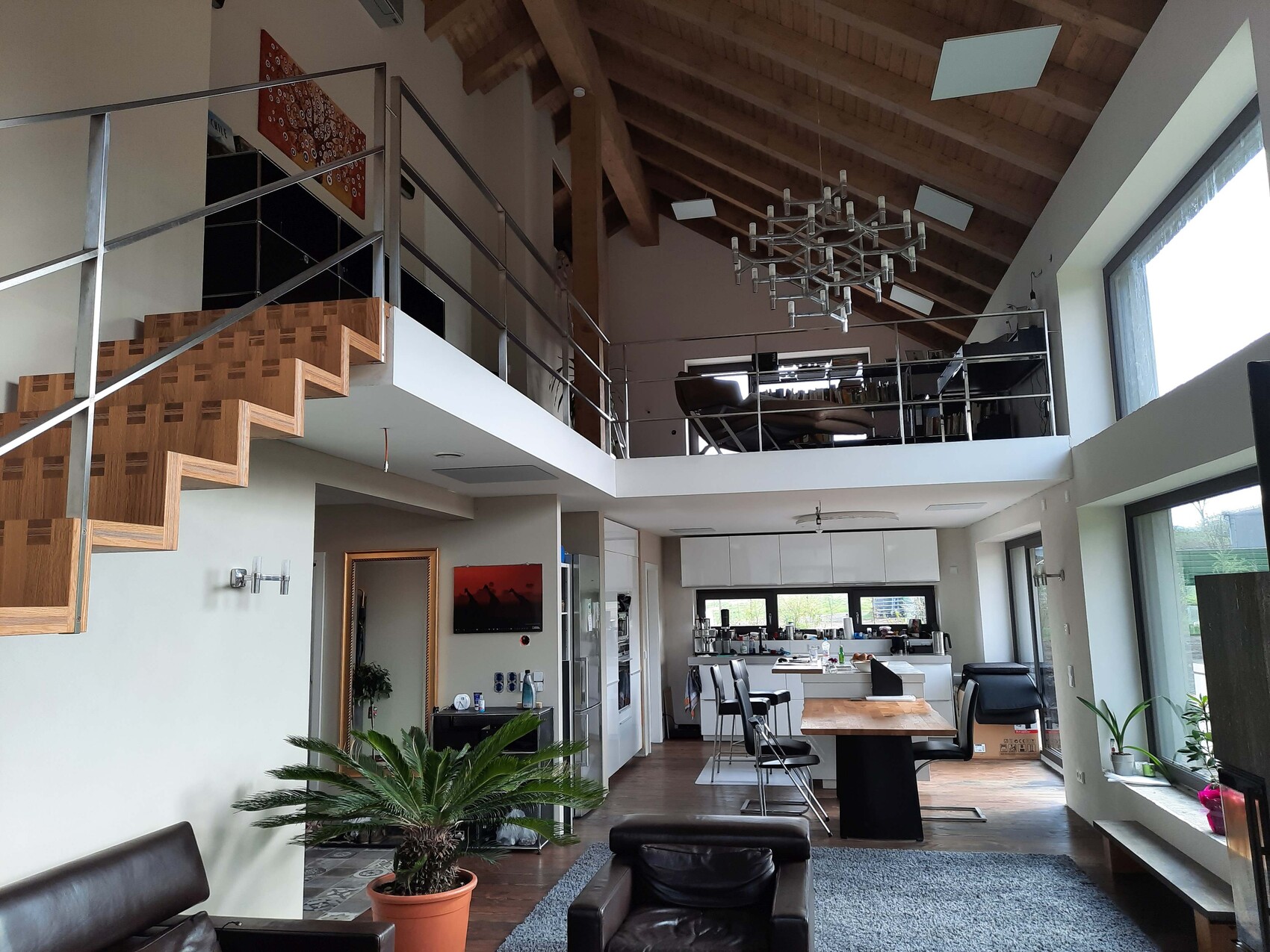 Open living loft with wooden staircase, roof structure, kitchen, and dining area on the ground floor.