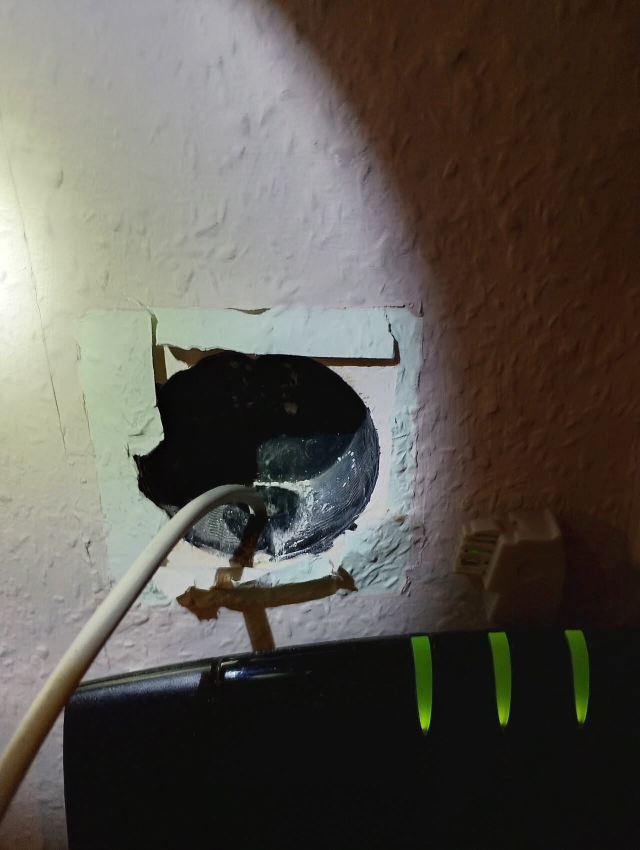 Hole in interior wall with pipe and cable, plaster crumbling around the hole