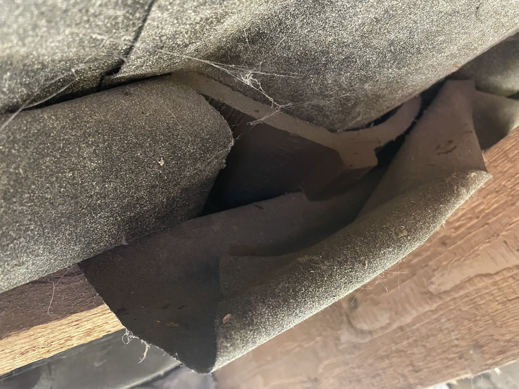 Close-up of dusty bitumen roofing felt and wooden beams in a roof structure.