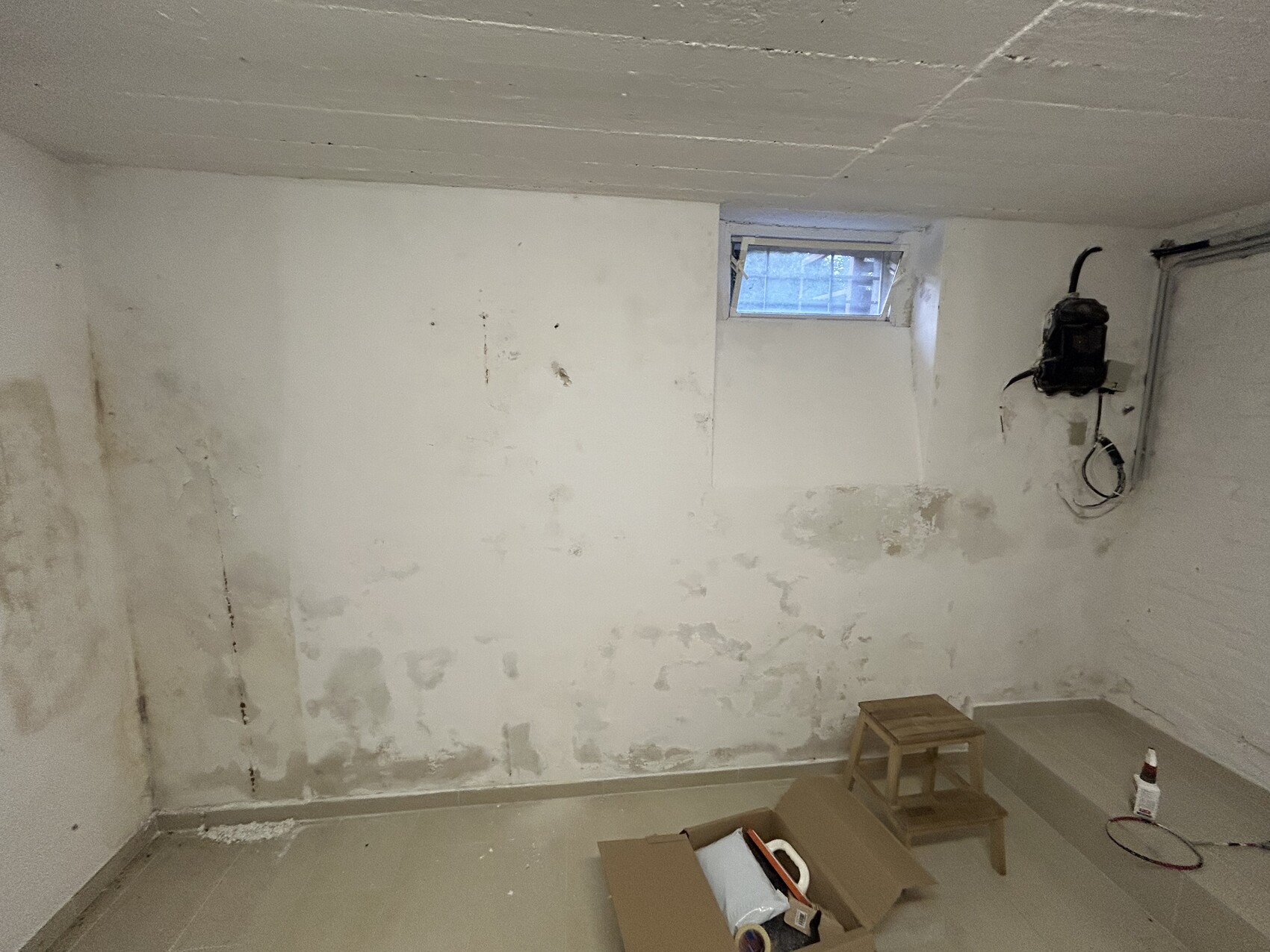 Basement room with rough, unpainted walls, small window, and construction tools