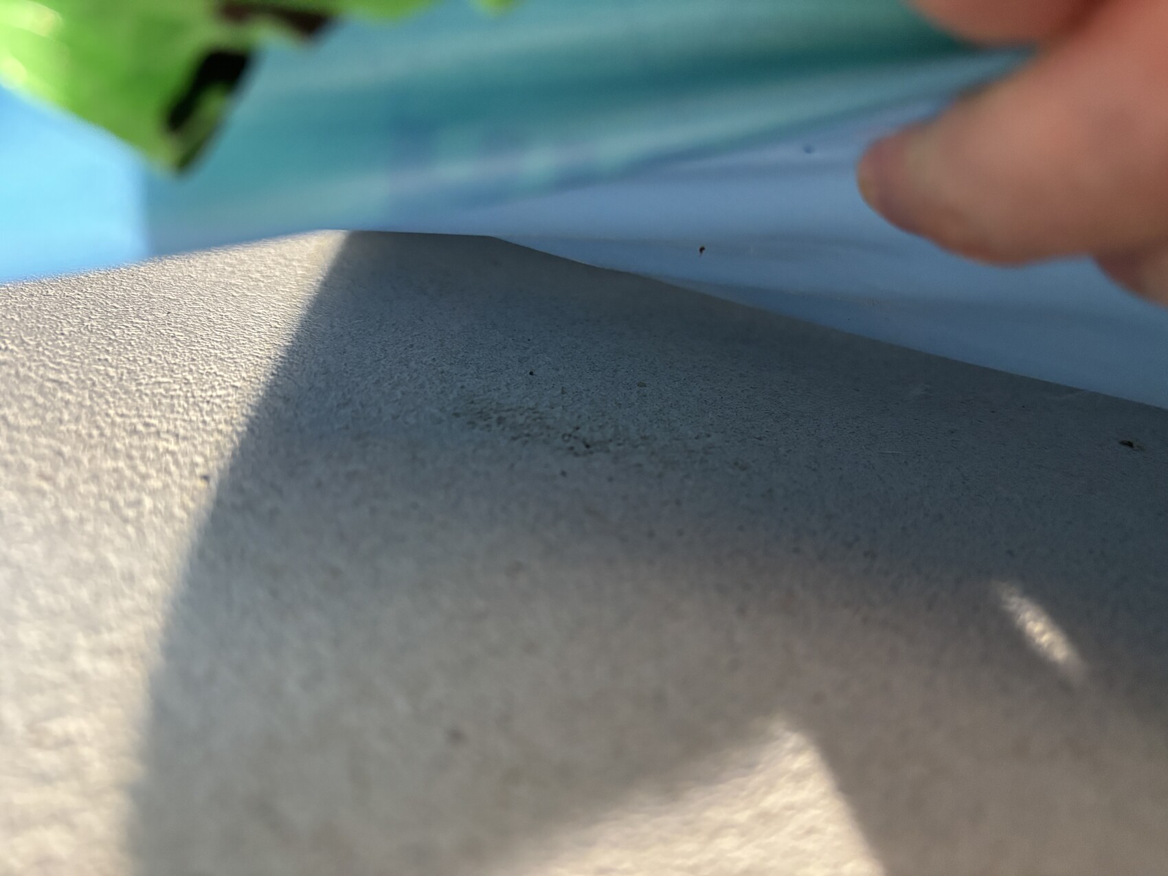 Close-up of a rough concrete surface with blue background and finger at the edge