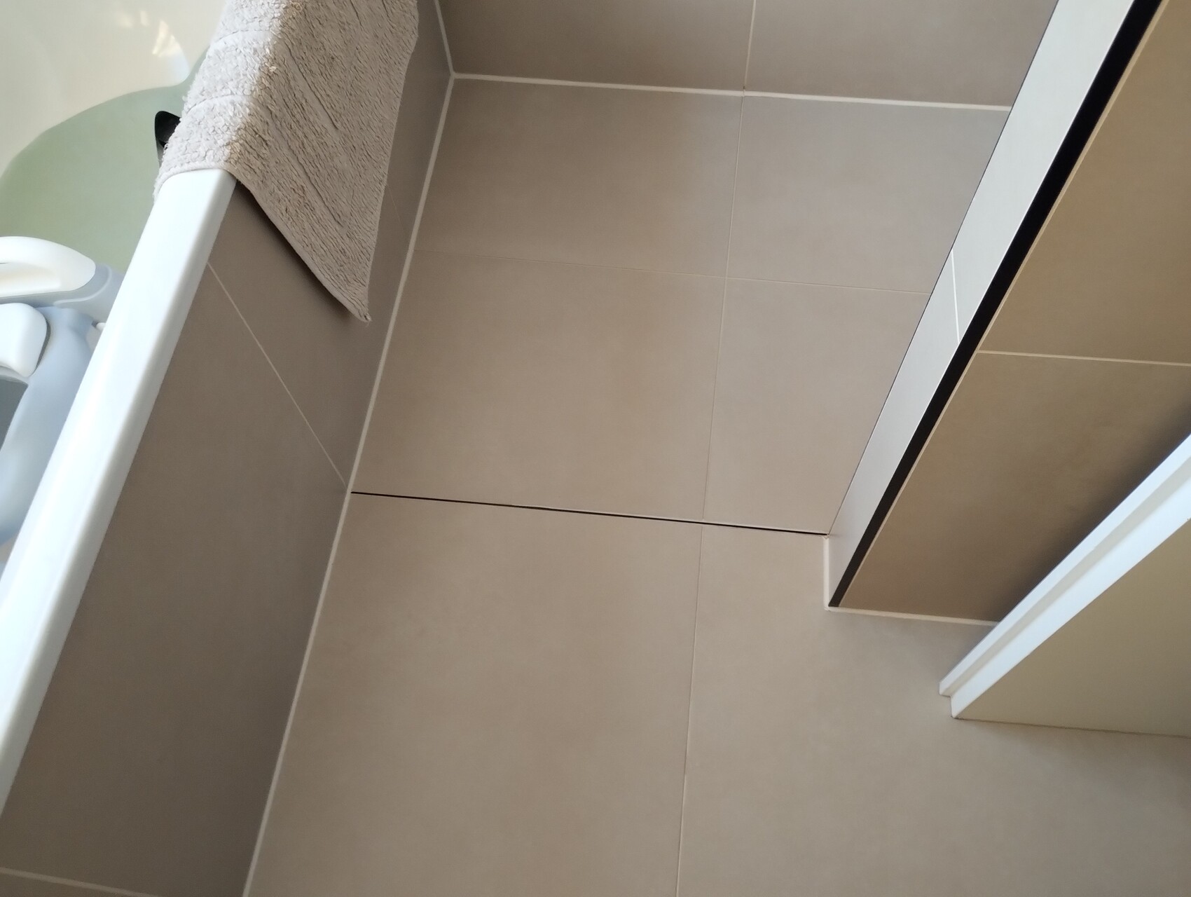 Beige bathroom with large floor tiles, bathtub edge and shower door.