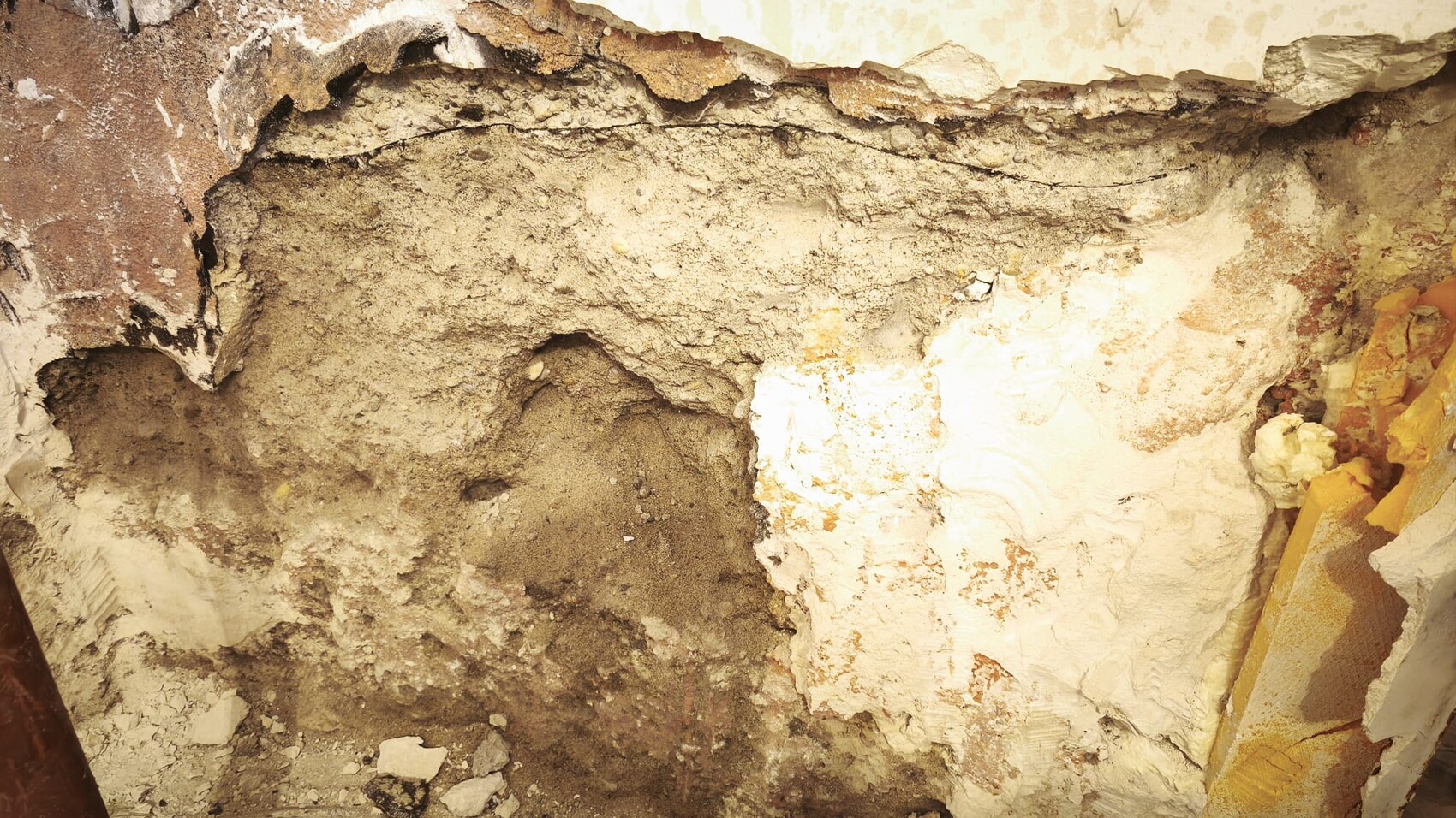 Exposed wall with plaster damage, earthy material and visible construction defects inside