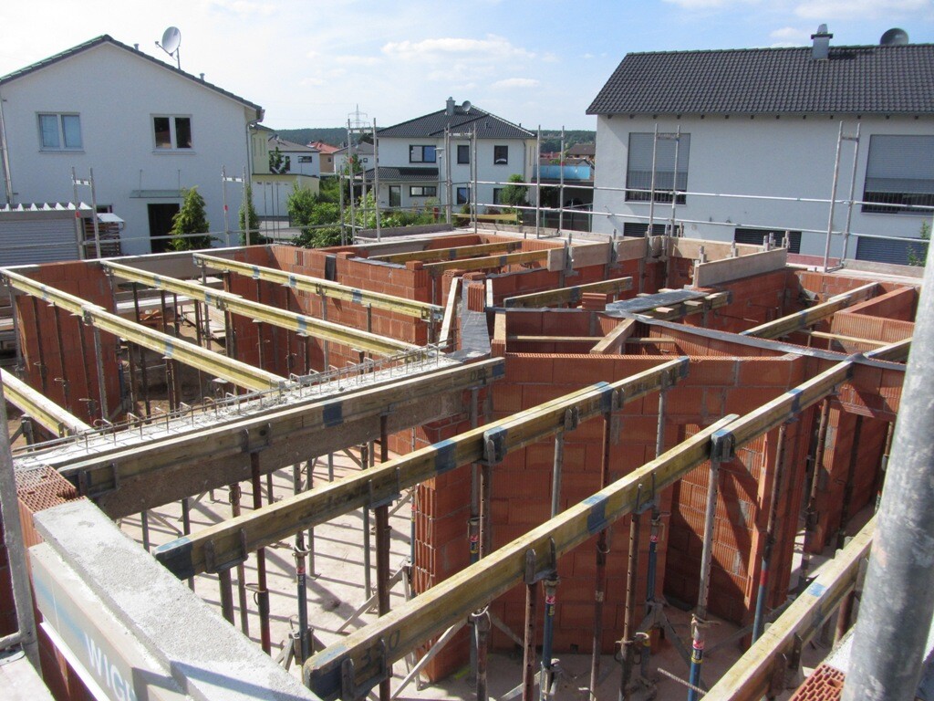 Construction site with red brick masonry, wooden supports, and scaffolding in a residential area.