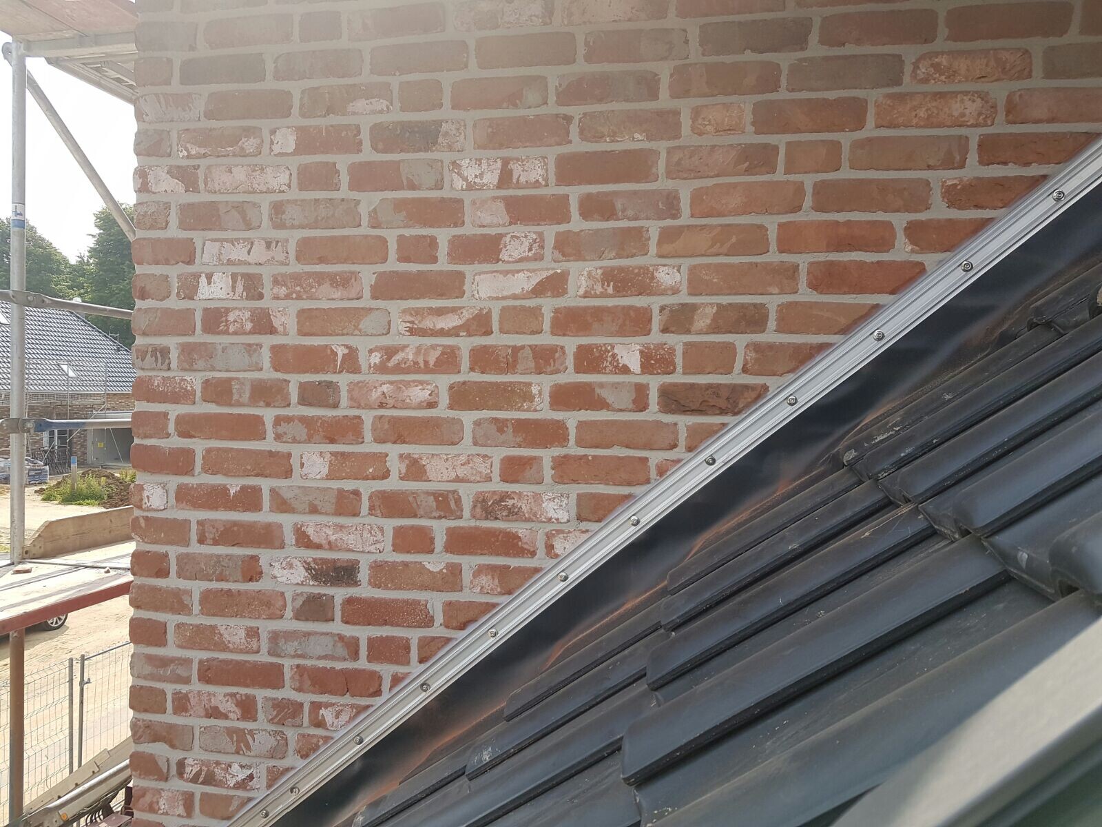 Brick wall of a construction project with scaffolding on the left, sloping roof in the foreground.
