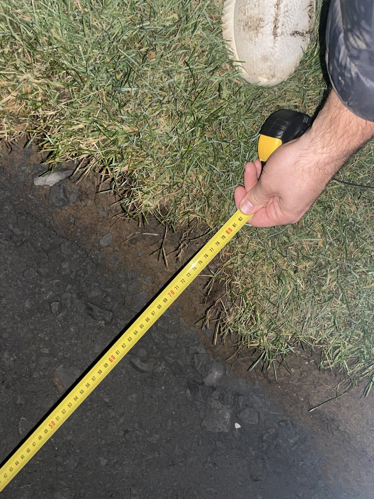 Person measuring construction property with tape measure on grass and soil surface.