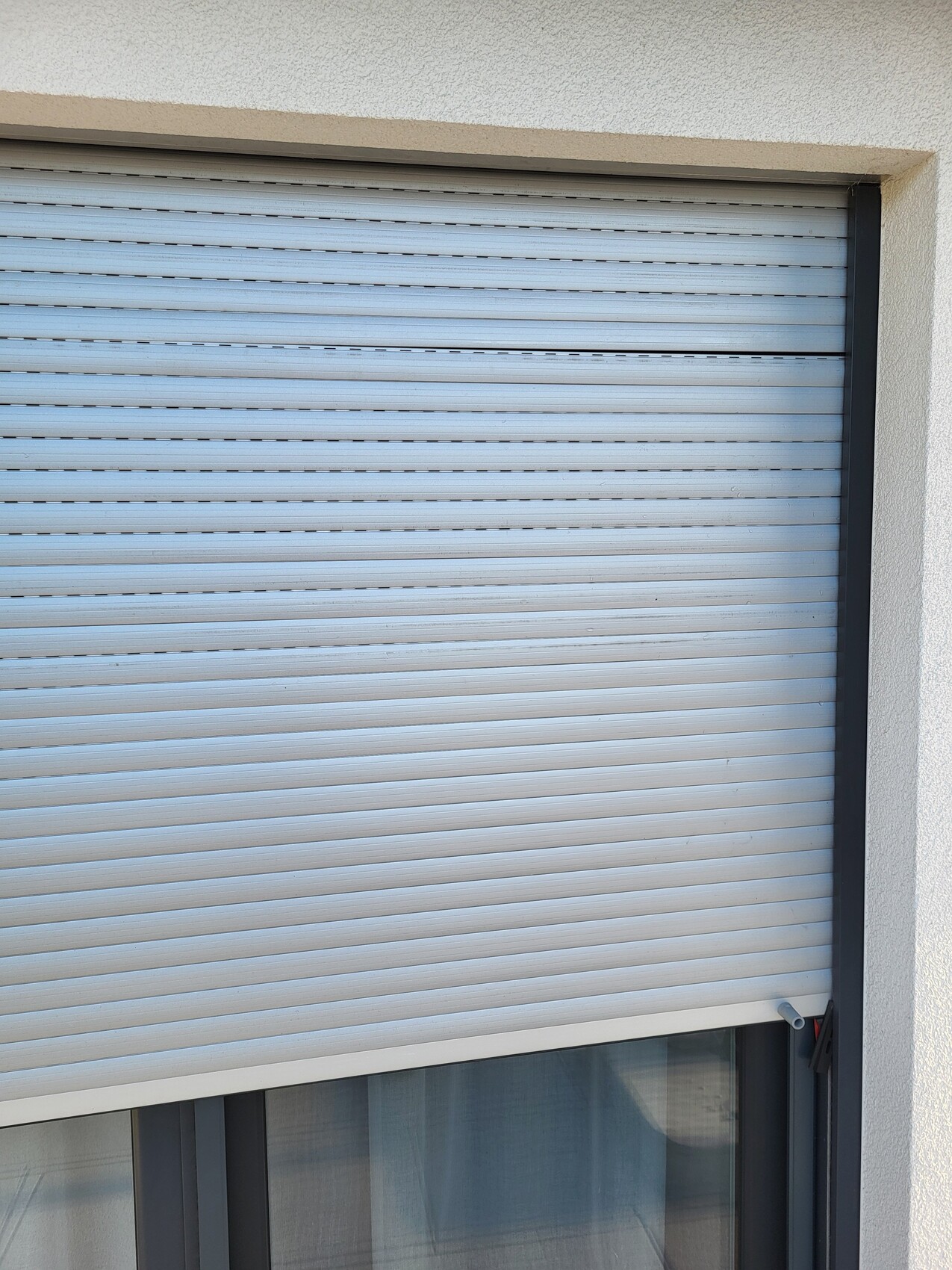 Exterior roller shutter in front of a window, white facade wall, shutter closed