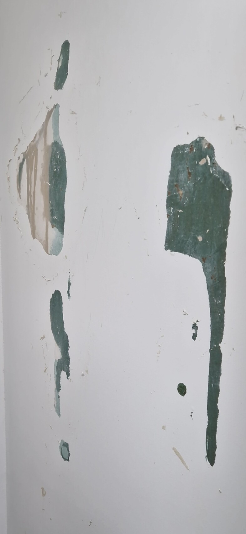 White interior wall with peeling green-blue paint and plaster spots