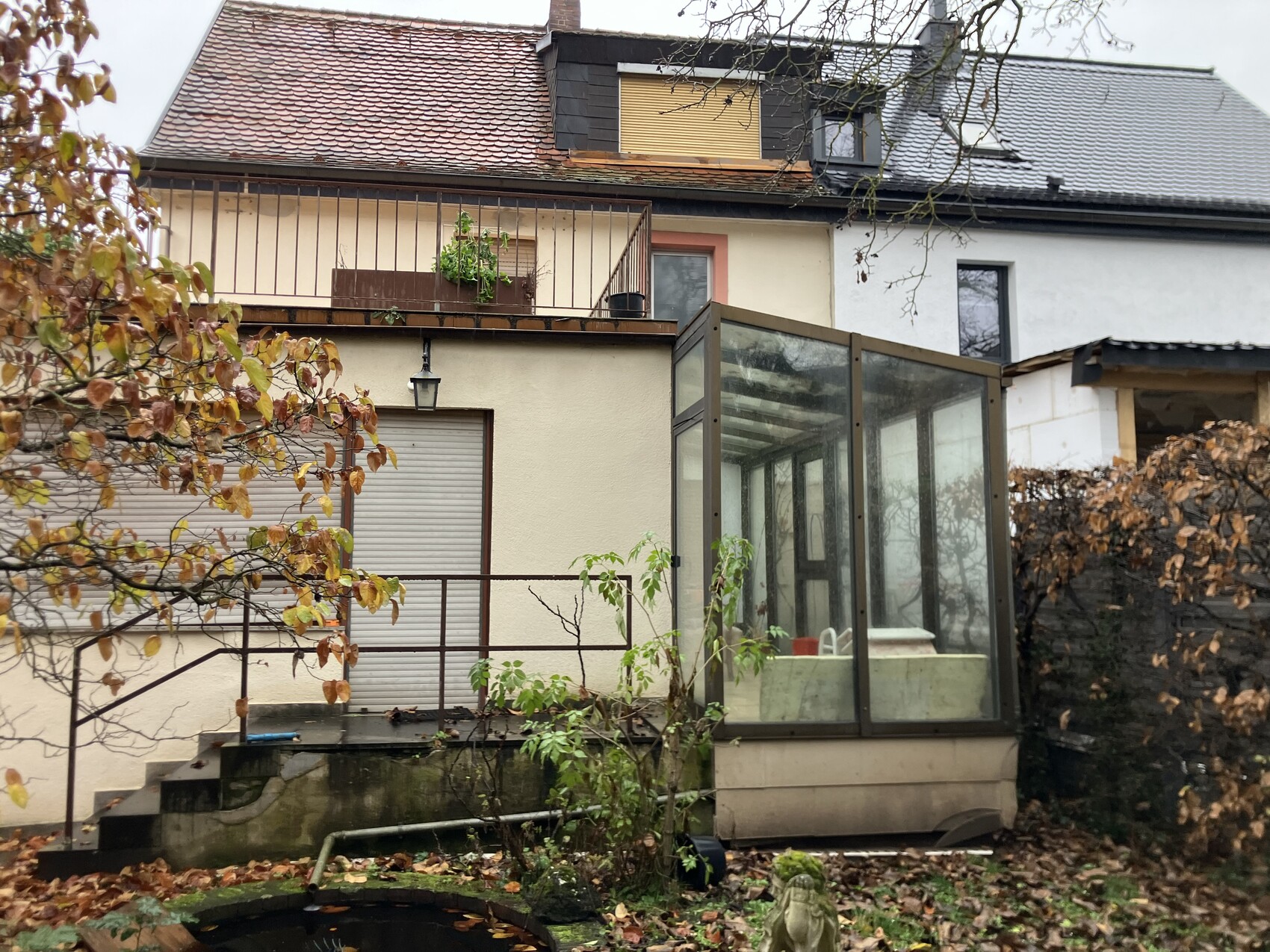 Außenansicht eines Hauses mit Glasveranda, Terrasse und Herbstlaub im Garten.