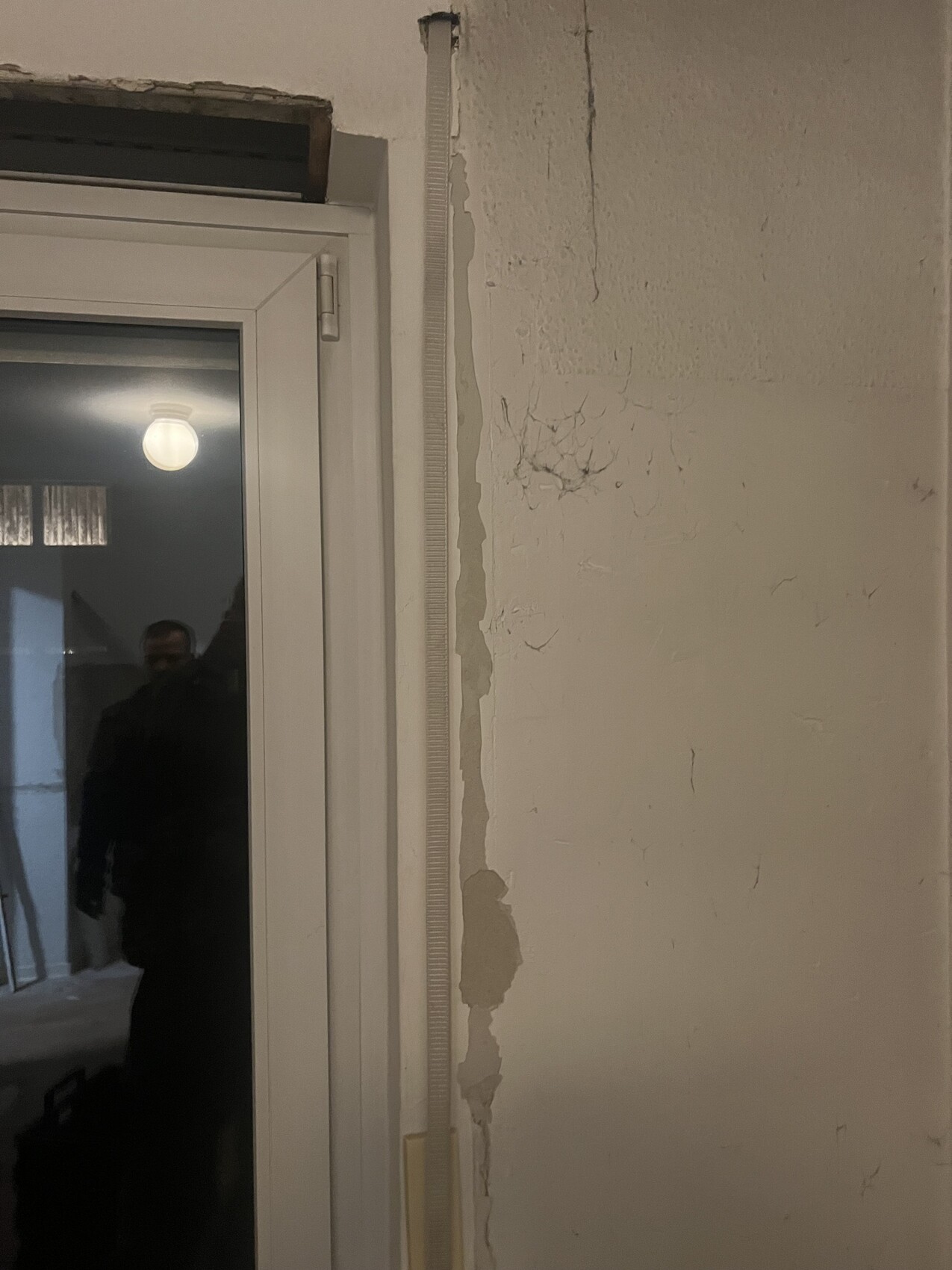 Interior with peeling plaster on the wall next to a door, uneven wall surface