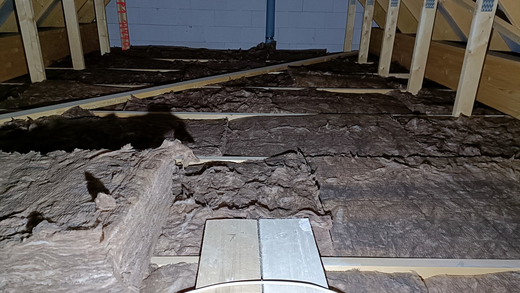 Unfinished attic with wooden studs and dark mineral wool insulation