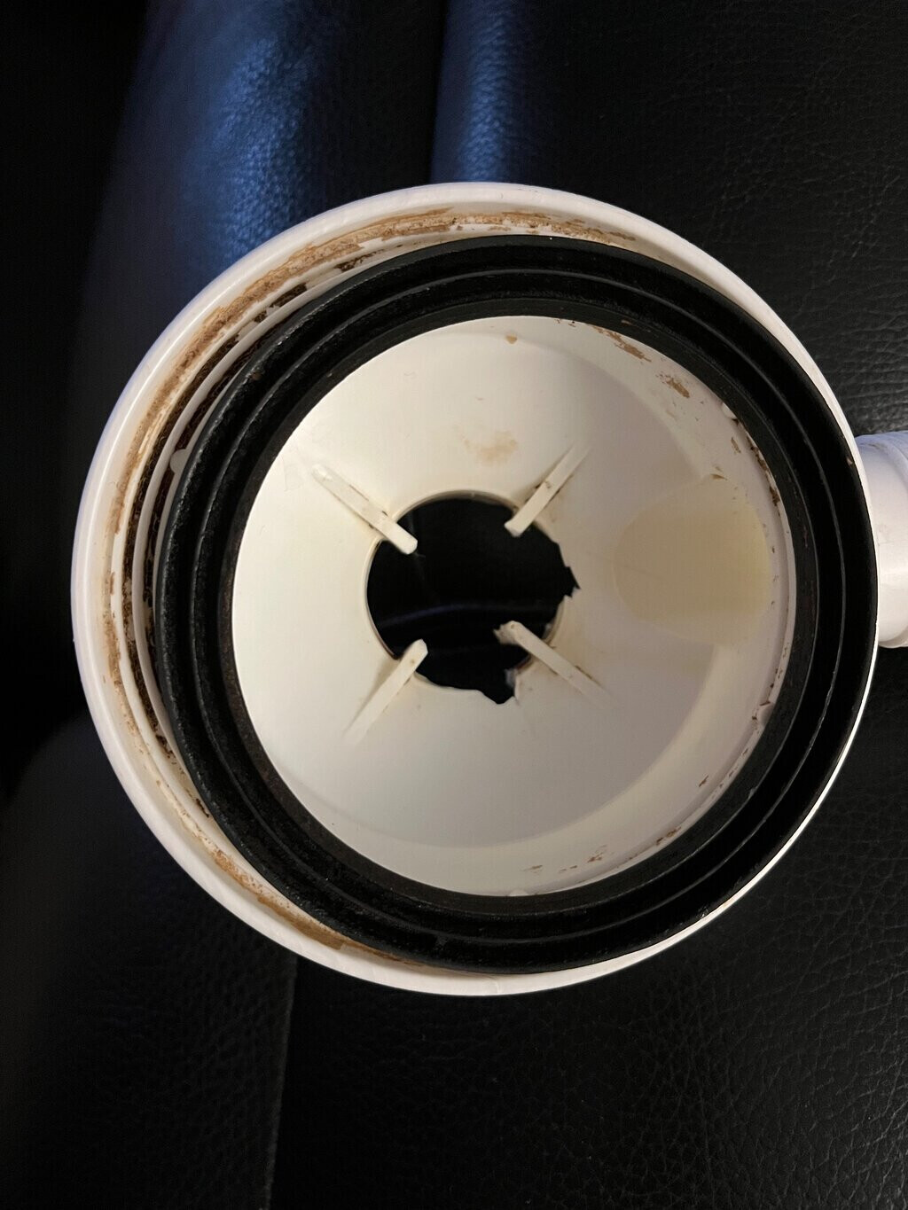 White plastic lid of a drinking container with a hole and brown stains, interior view