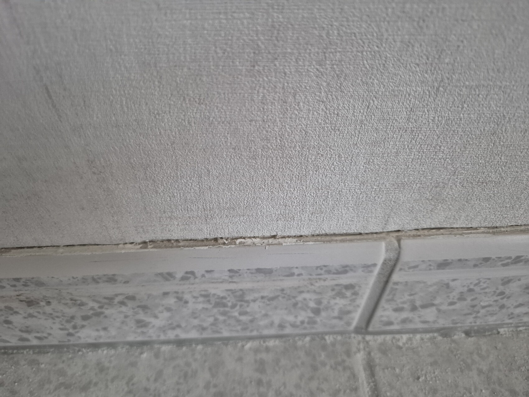 Close-up of the joint edge between tiled floor and wall with dust and irregularities.