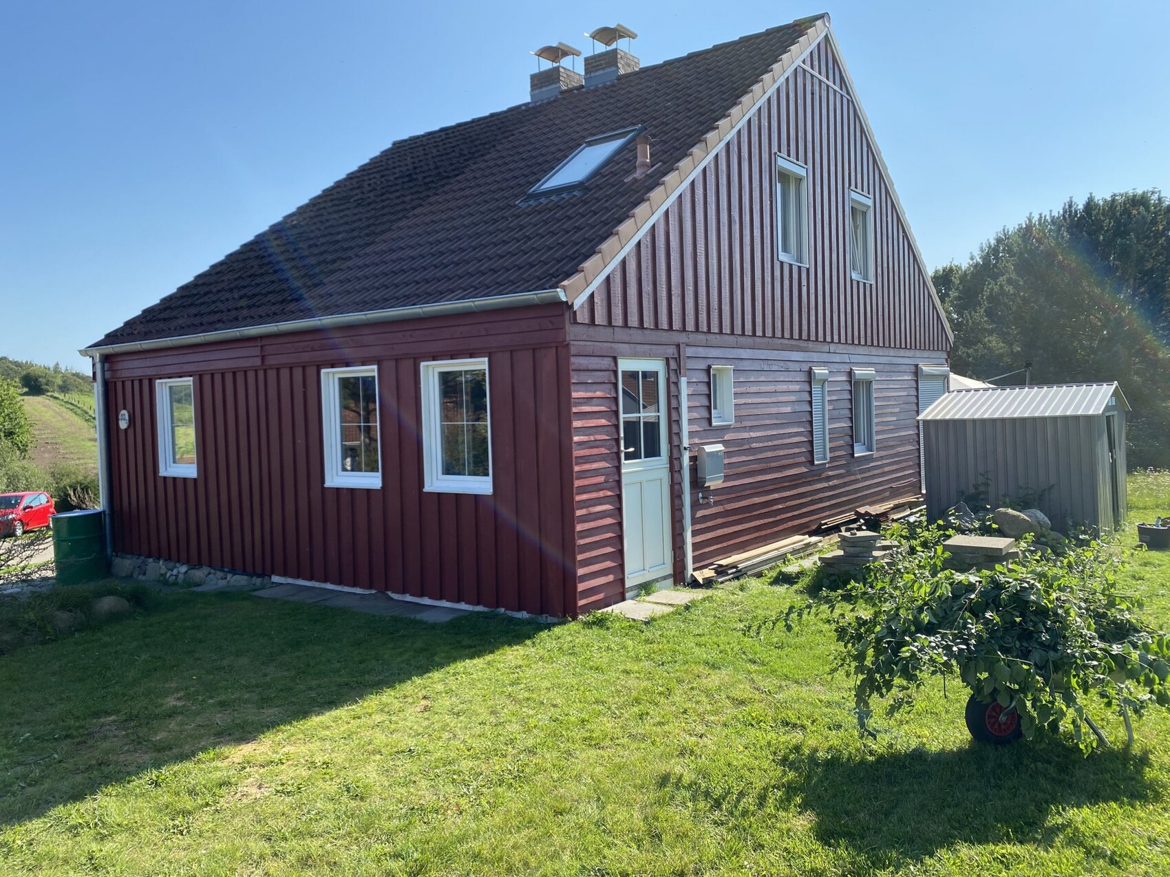 Wood-clad house from the outside with red siding, white windows, and garden