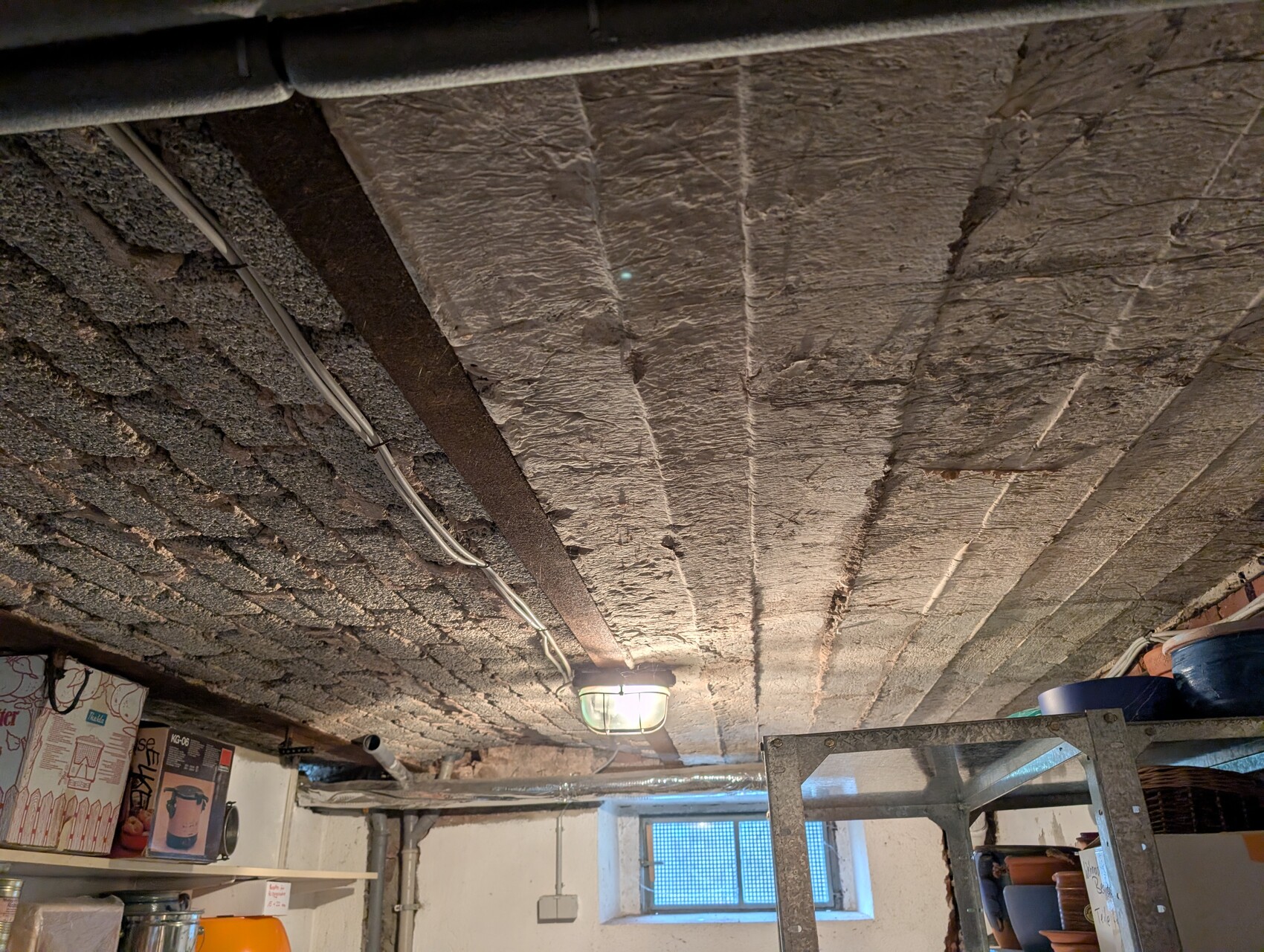 Basement ceiling with insulation, visible cables, ladder and construction materials in basement room