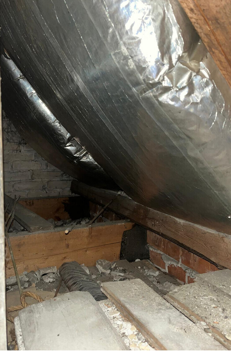 Attic with aluminum foil insulation, wooden rafters, and building materials, untidy