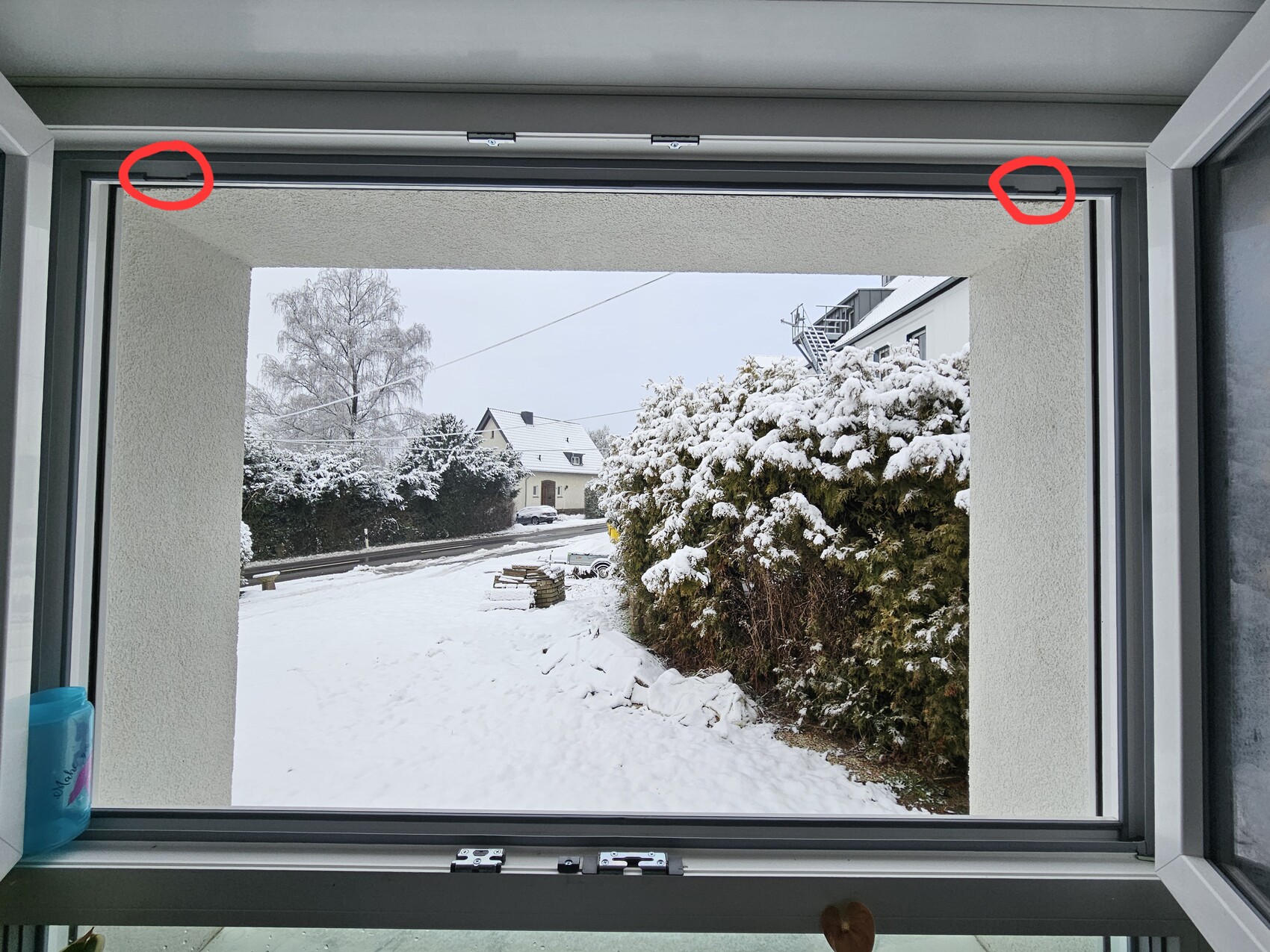 Window view of snow-covered street scene with hedges and houses in winter