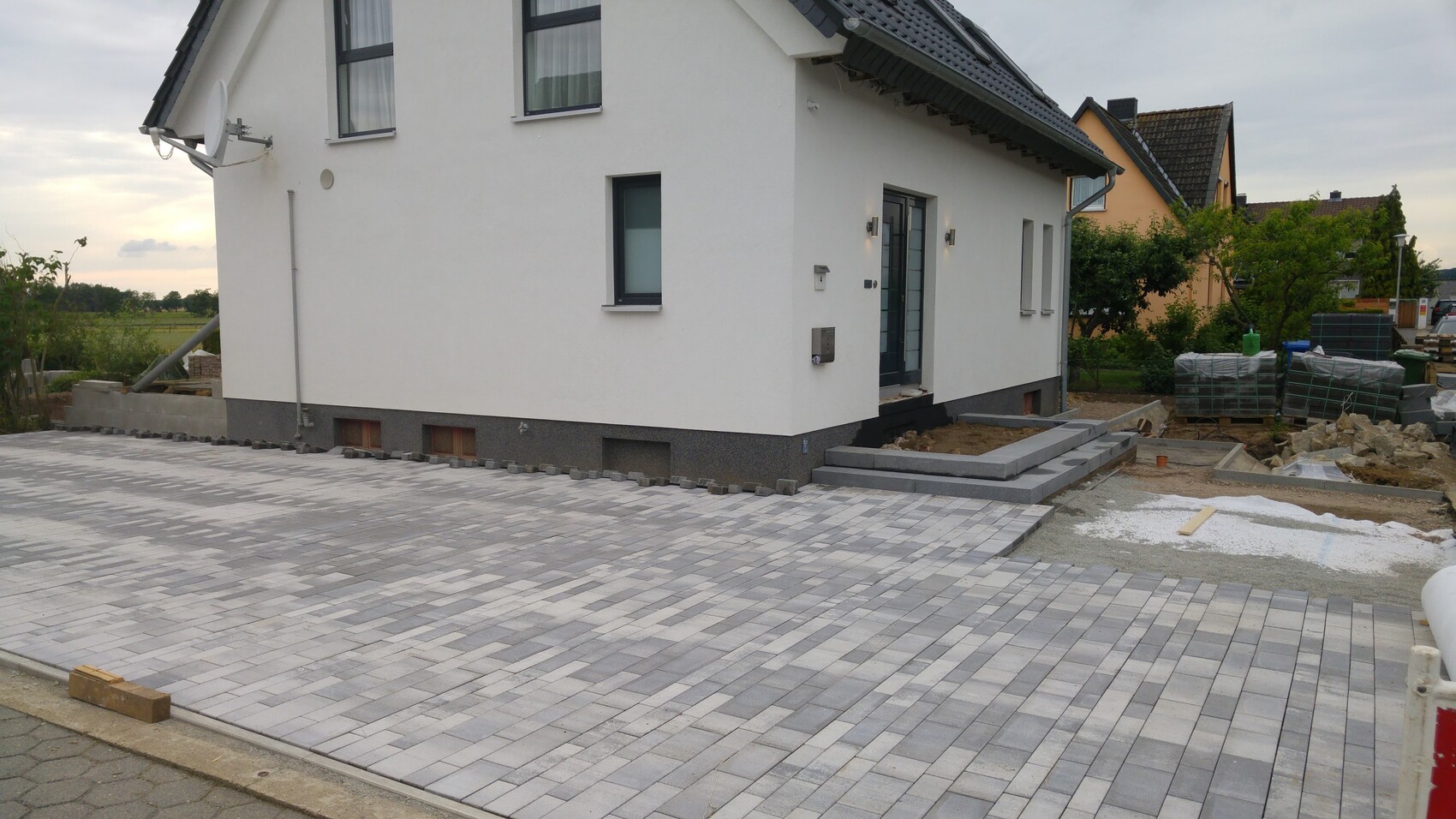 Modern white detached house with gray paved area in the front yard; construction materials visible.