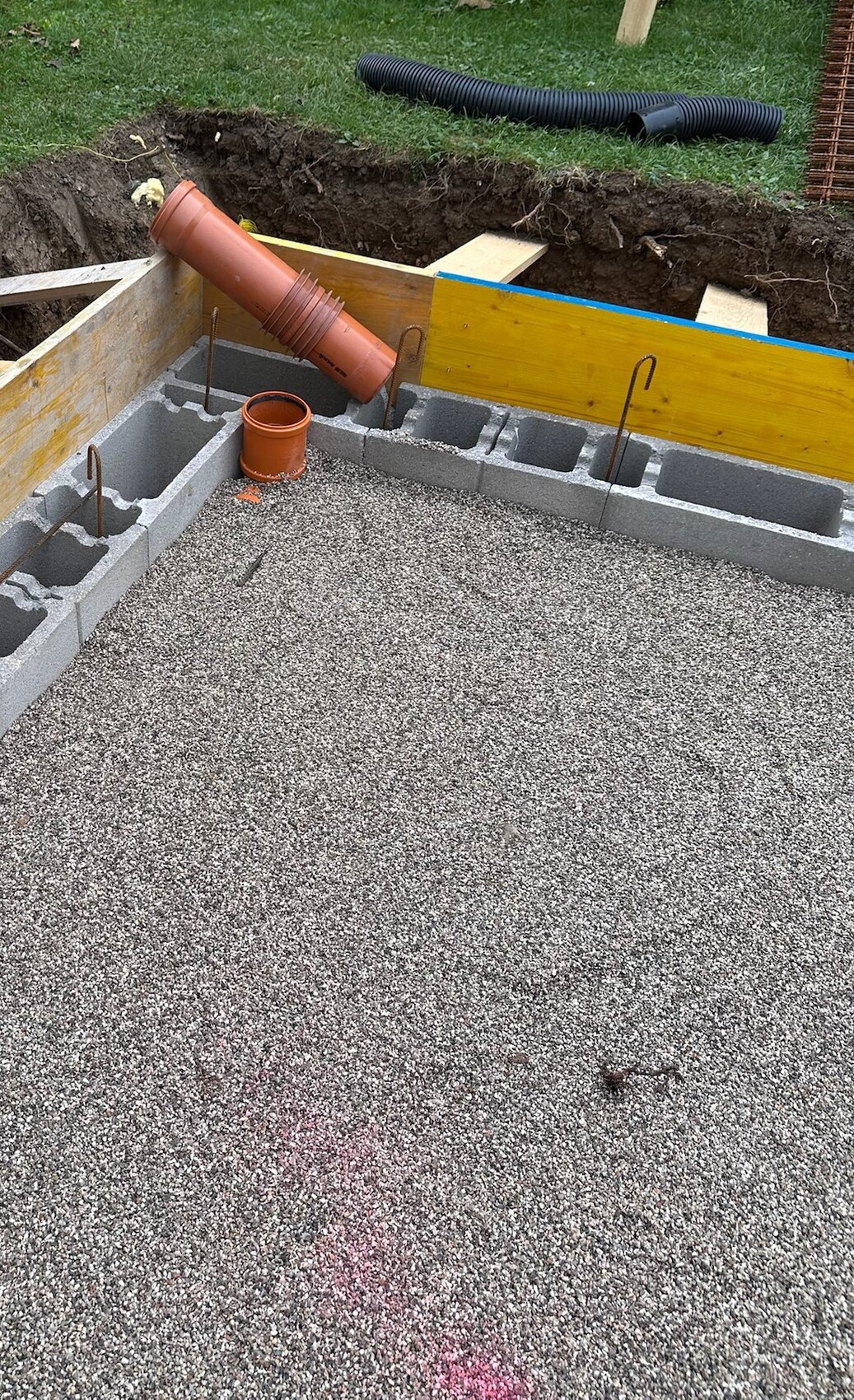 Baustelle mit Fundamentsteinen, Abwasserrohr und Schalung für Rohbaufundament.
