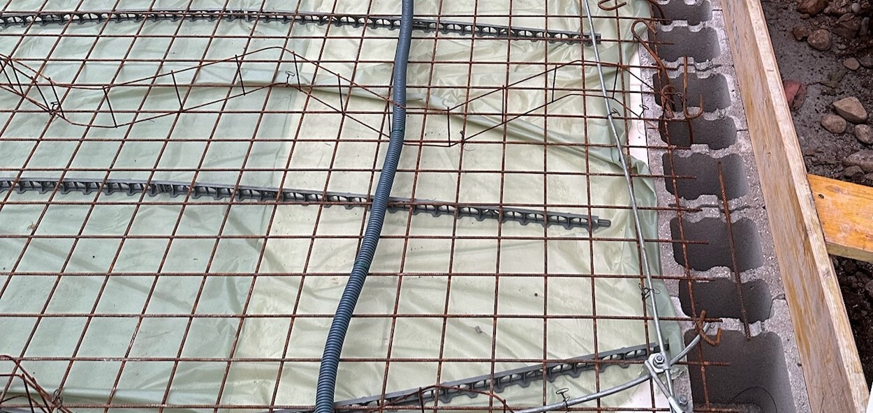 Baustelle mit Bewehrungsstahlgitter auf Fundamentfolie und Rohbauarbeiten im Erdreich
