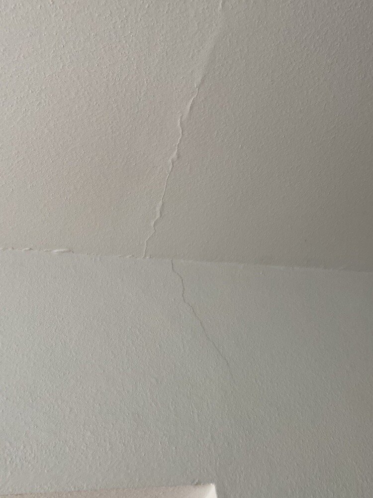 Wall and ceiling crack visible indoors, fine cracks at the corner