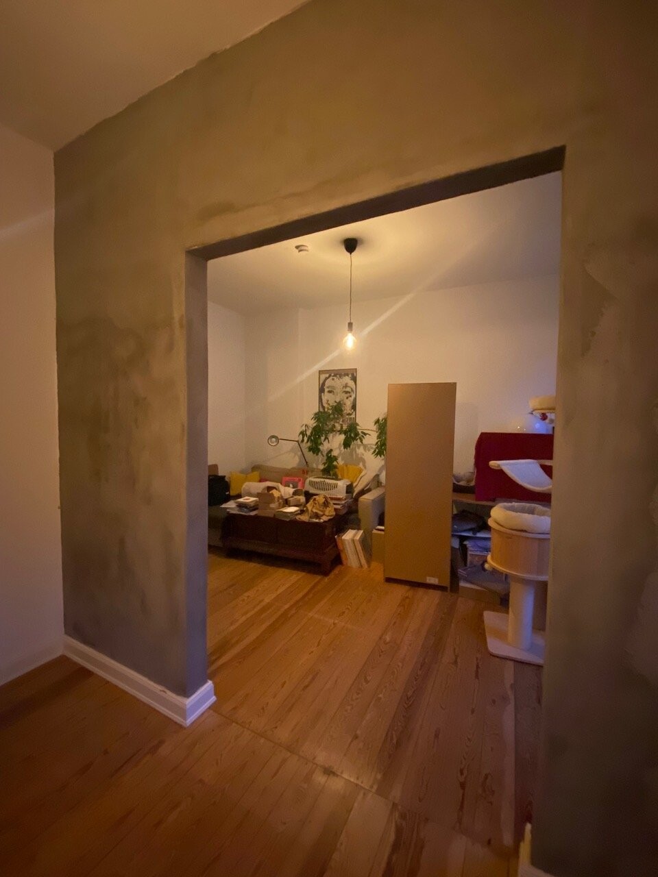 Living area under renovation with raw walls, wooden floor, and a chaotic collection of furniture